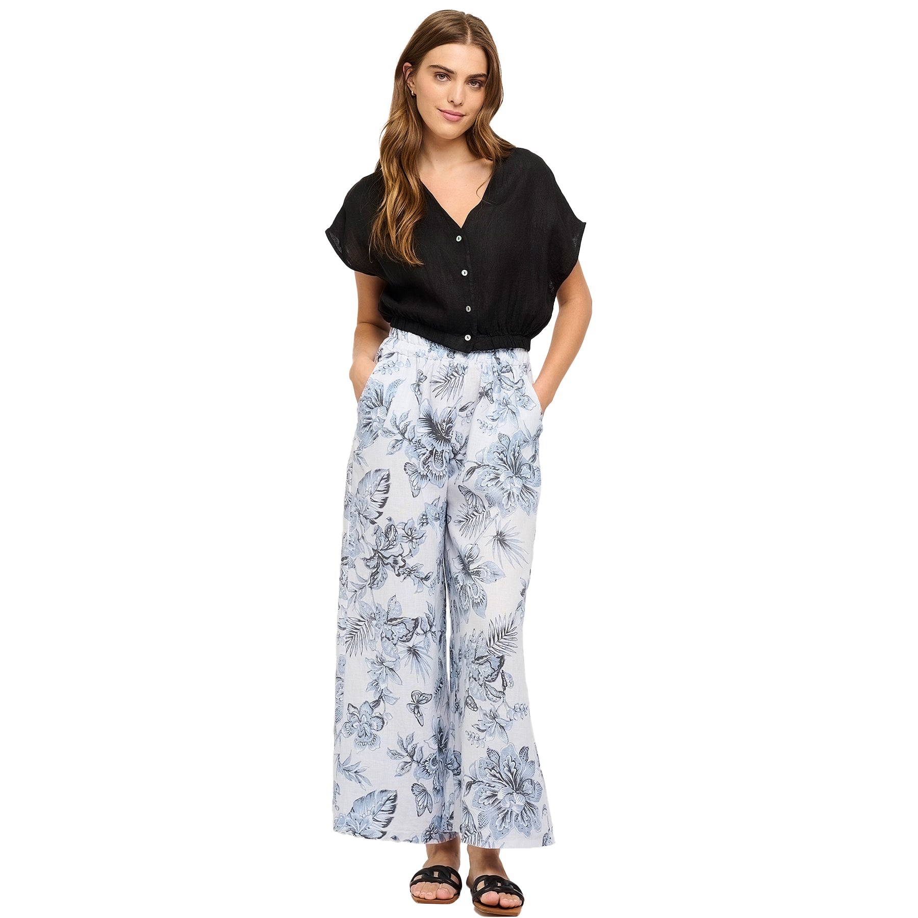 Woman wearing powder blue floral wide-leg linen pants with side pockets, paired with a black short-sleeve blouse - relaxed warm-weather outfit.