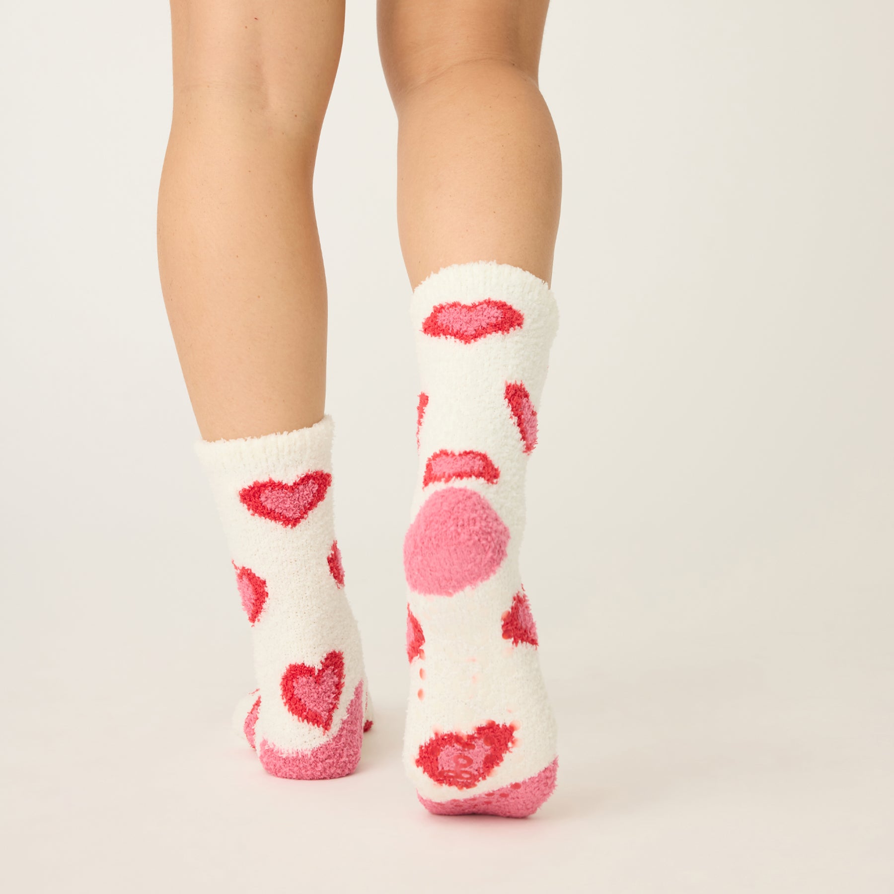 White socks with pink heart patterns worn by a person on a light beige background