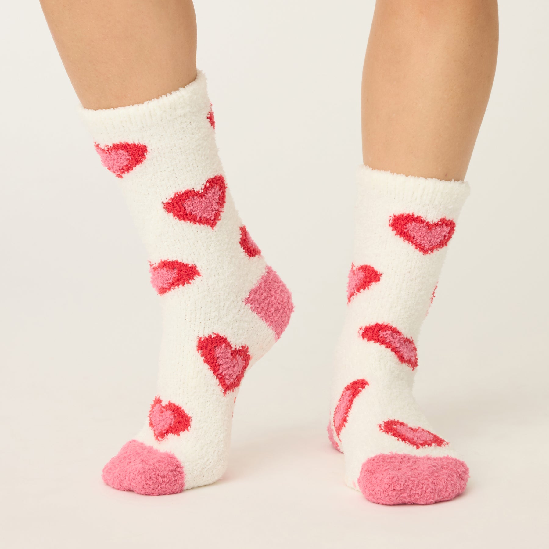 White socks with red hearts worn by a person on a light beige background