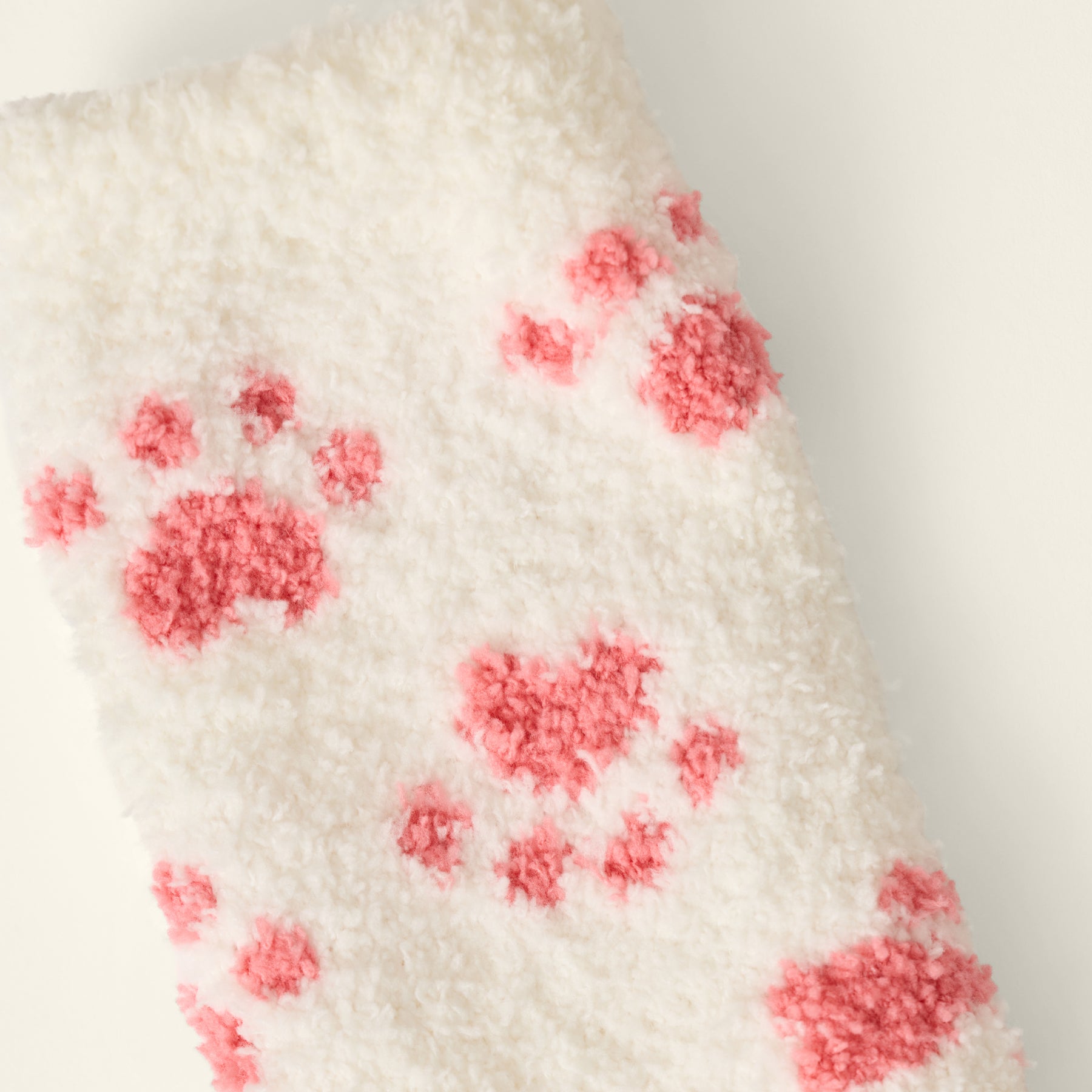 Close-up of ivory fuzzy sock fabric featuring a playful pink paw print pattern.