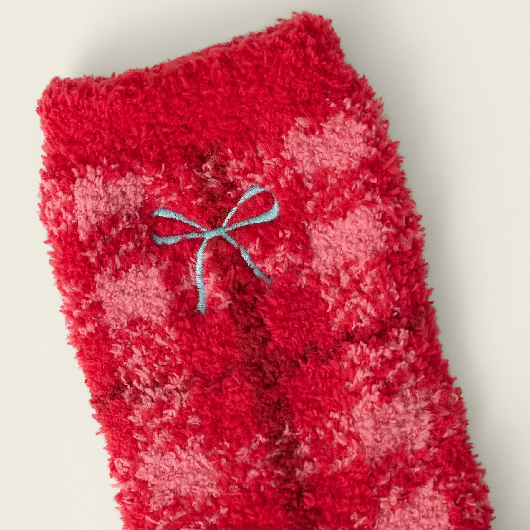 Close-up of red and pink plaid plush sock fabric featuring a small blue embroidered bow detail.