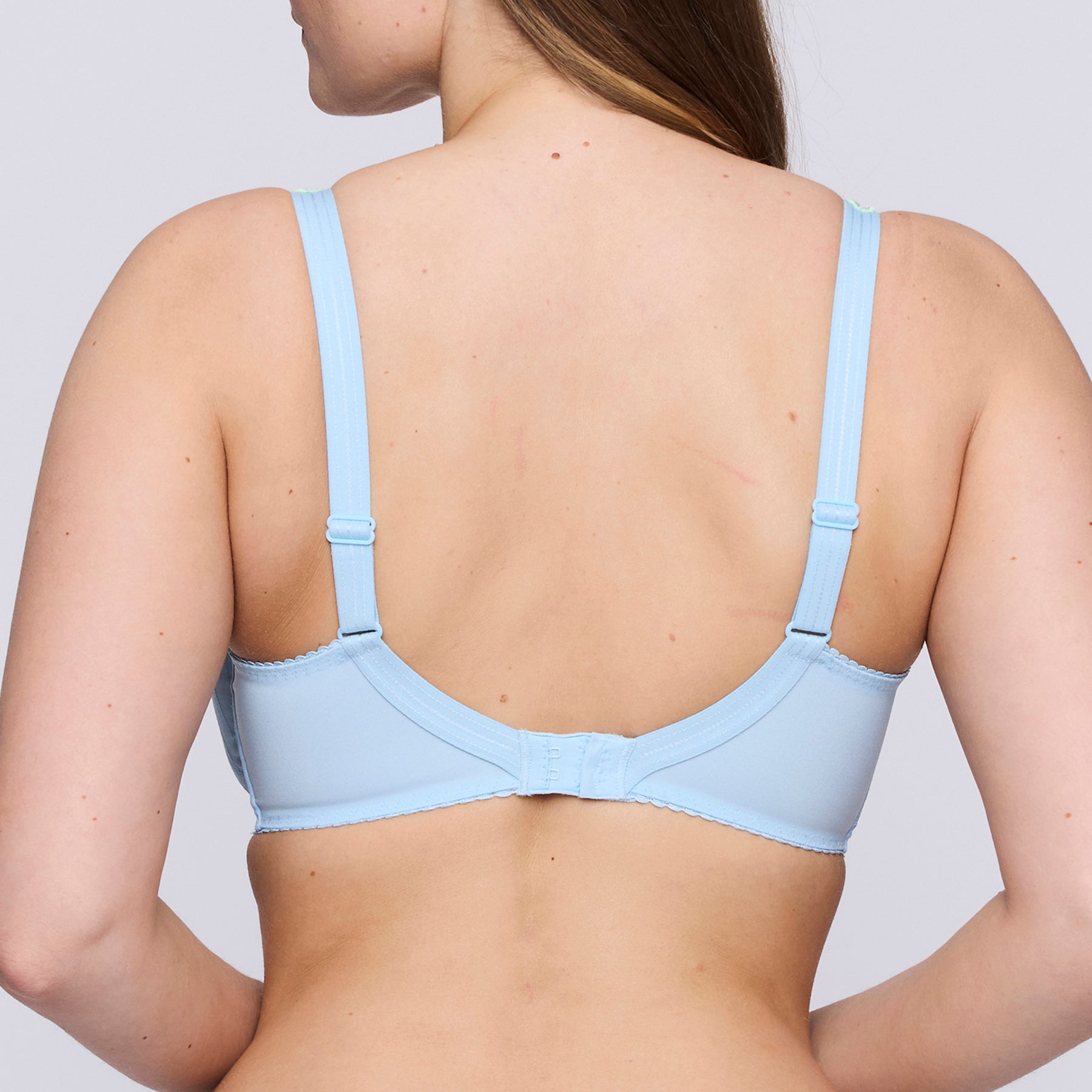 Full cup underwired bra in milky baby blue with contrast lime green embroidery on upper cups. Rear view on model.
