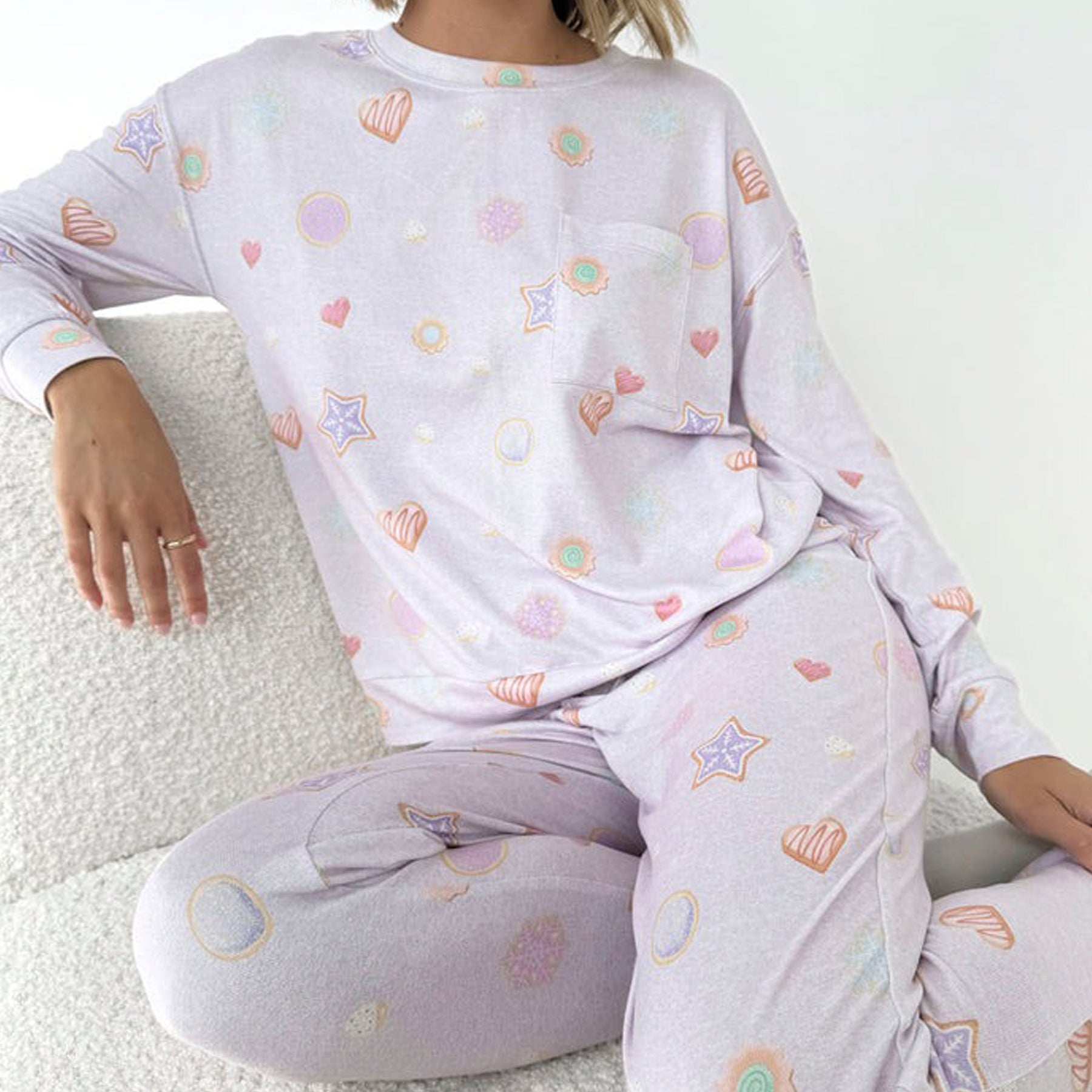 Woman wearing pastel lilac pajama set with candy and heart prints, sitting on a chair.