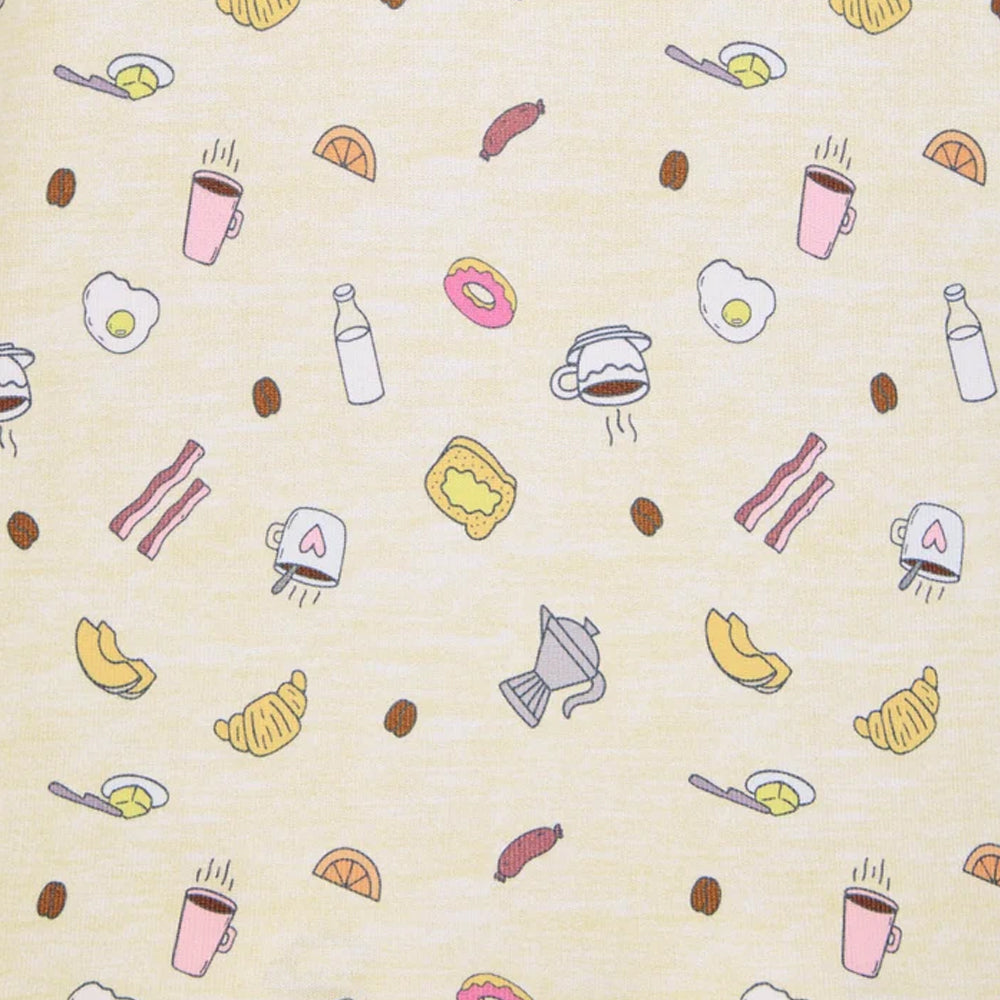 Close-up of Splendid Pillowsoft pajama fabric featuring coffee cups, croissants, eggs, bacon, donuts, and breakfast illustrations on a cream background.
