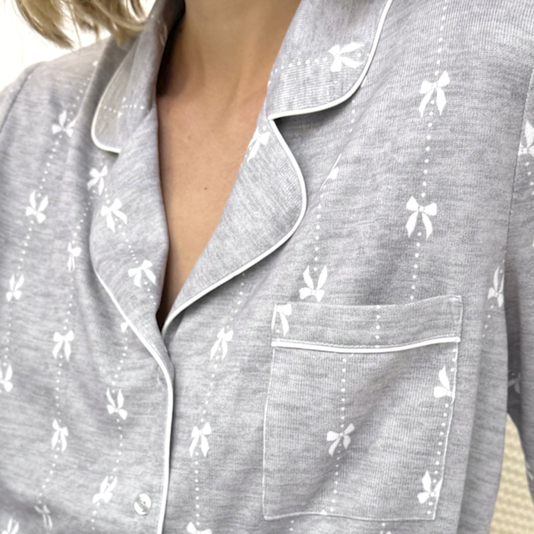 Close-up of grey pyjama top with white bow print, white piping, and front pocket detail.