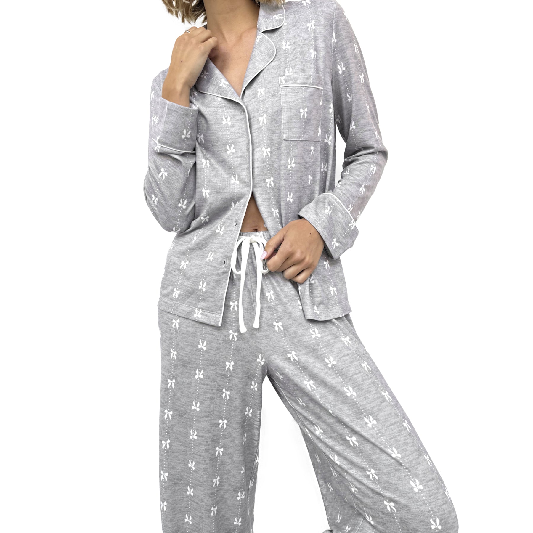 Woman wearing grey button-up pyjama set with drawstring pants and all-over white bow print.