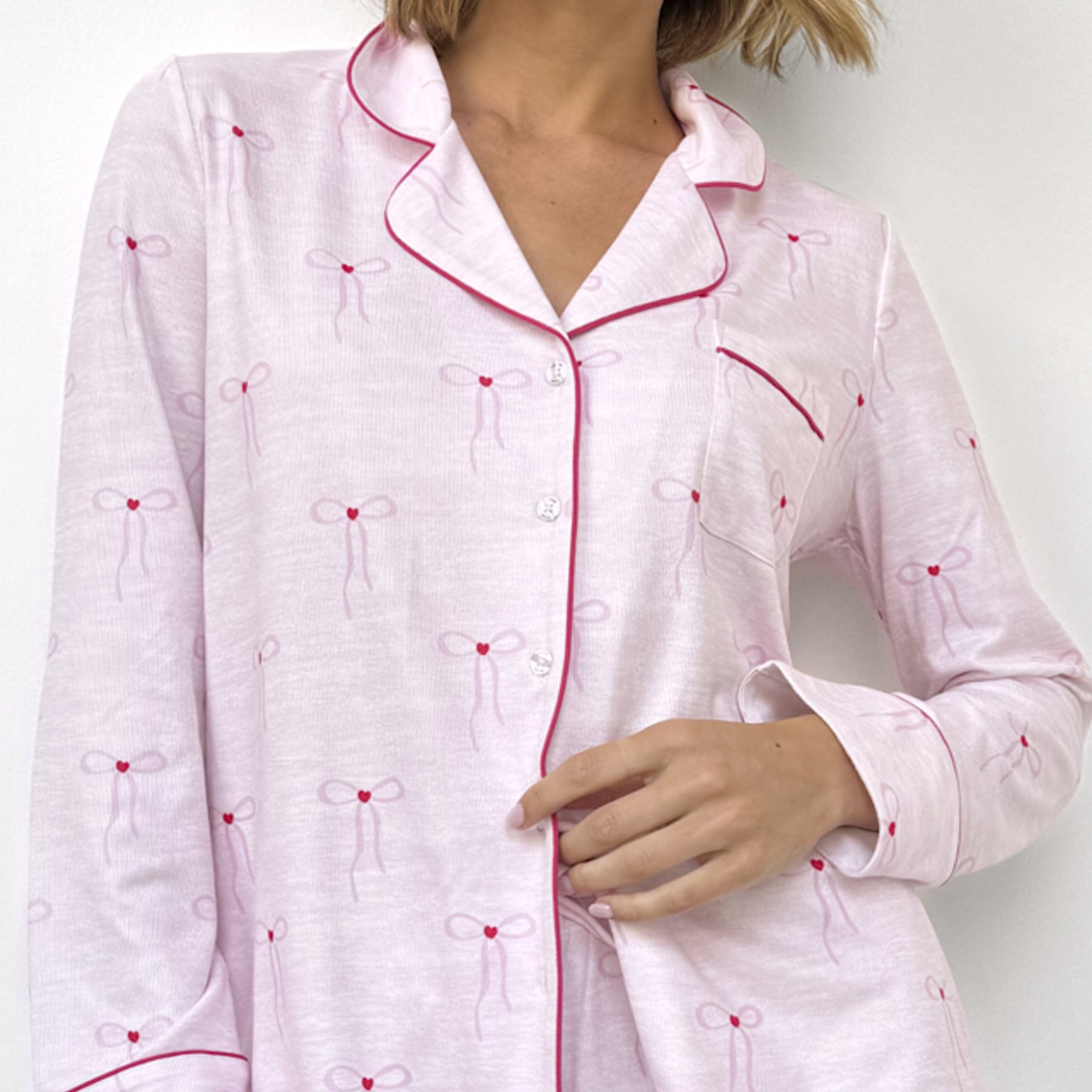 Detailed view of pink pyjama top with red bow print, button-up front, and red piping.