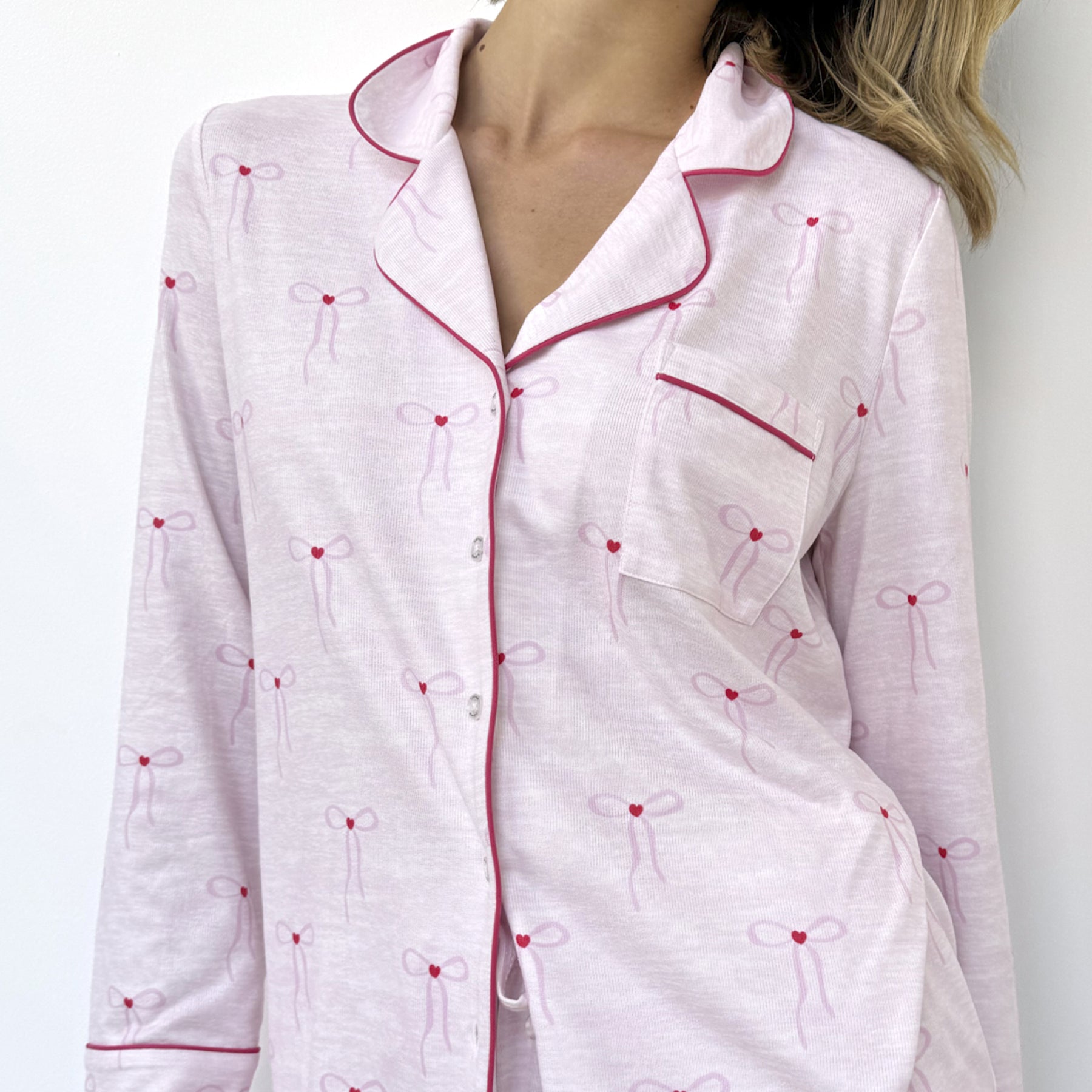 Close-up of pink pyjama top showing bow pattern, chest pocket, and soft red piping detail.