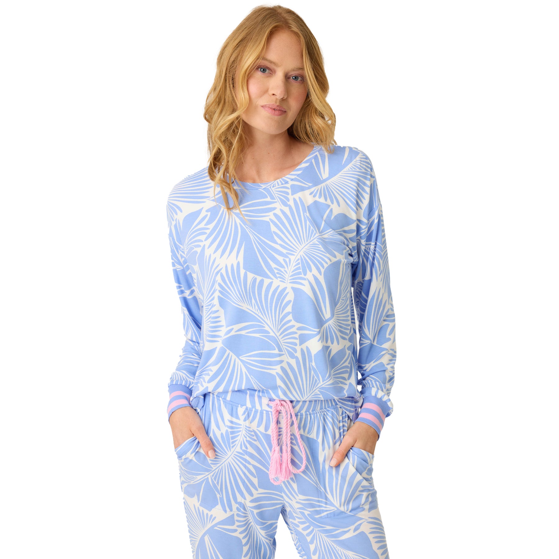 Woman wearing a blue and white tropical print lounge set with long sleeves and jogger pants, hands in pockets.