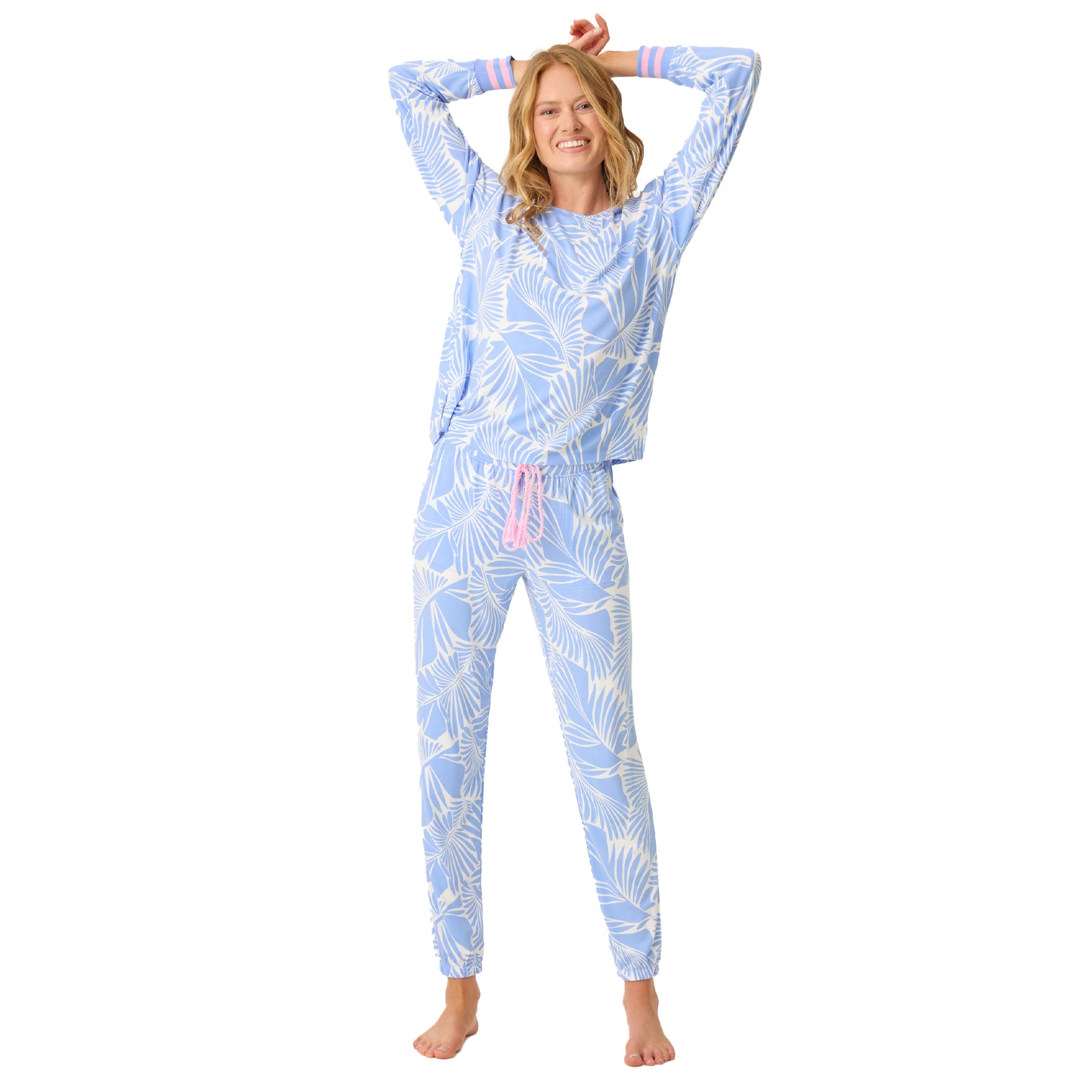 Full-body view of woman wearing blue and white tropical print loungewear set with pink drawstring, arms raised.