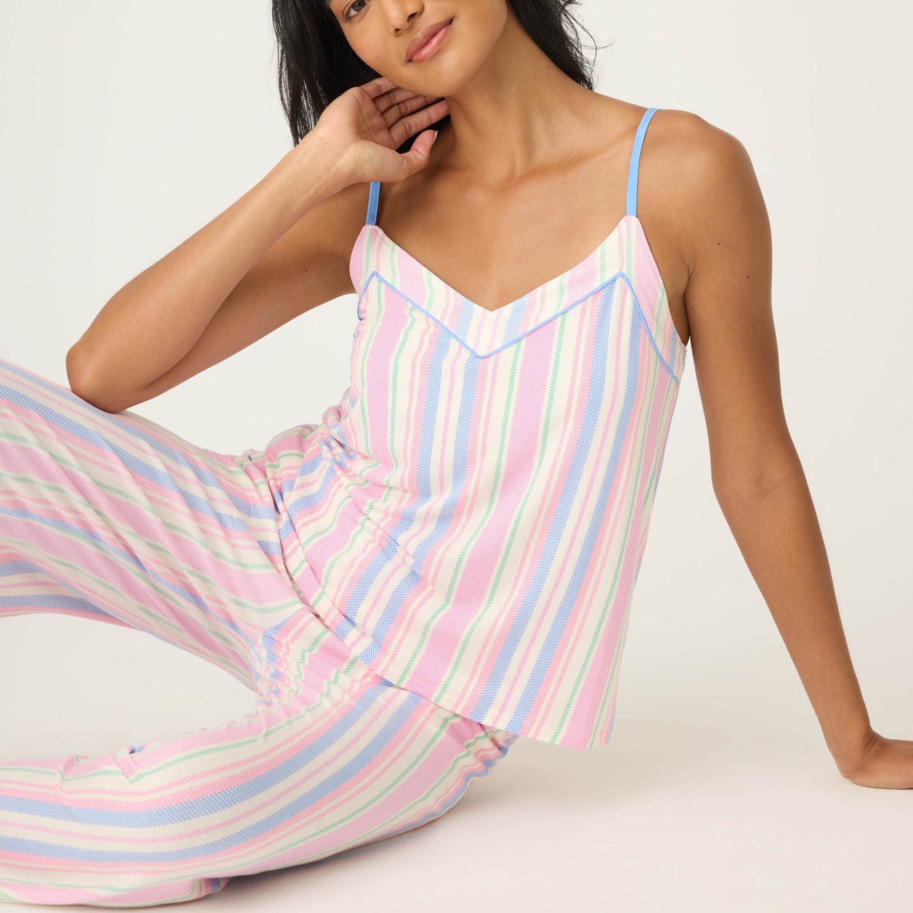 Woman sitting on the floor in pastel striped pyjama set with V-neck camisole and wide-leg pants.