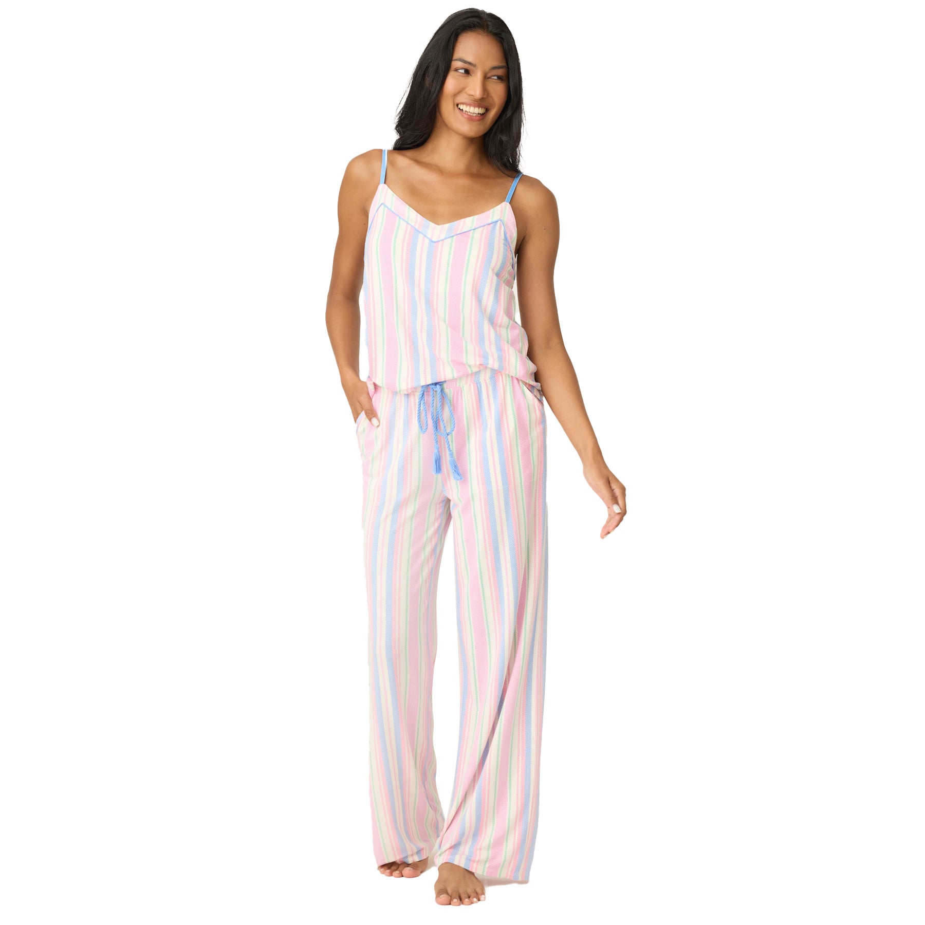 Woman standing with hands in pockets, wearing pastel striped pyjama set with blue adjustable straps and relaxed-fit pants.