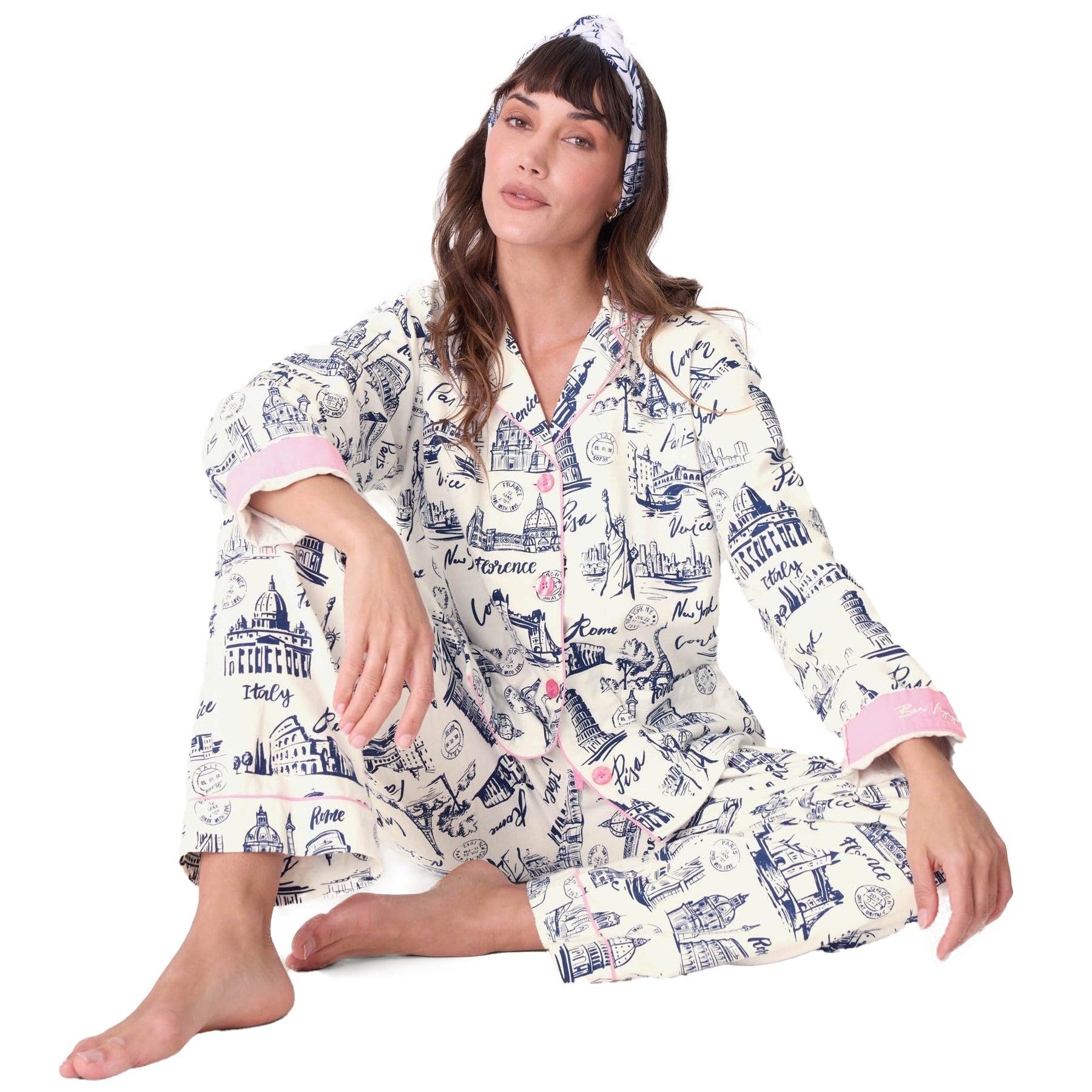 Woman wearing white pajama set with navy travel sketch print featuring world landmarks and pink piping accents.