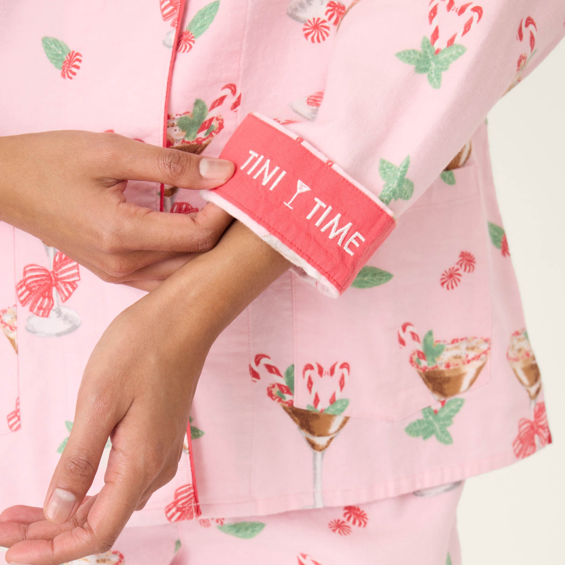 Person wearing a pink pajama set with candy cane pattern, holding a red card with 'TINI TIME' text.