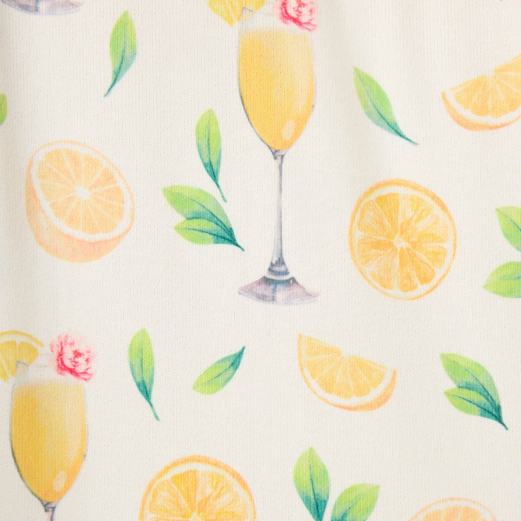 Close-up of ivory fabric with a colourful print featuring lemon slices, leafy sprigs, and mimosa cocktails in champagne flutes.