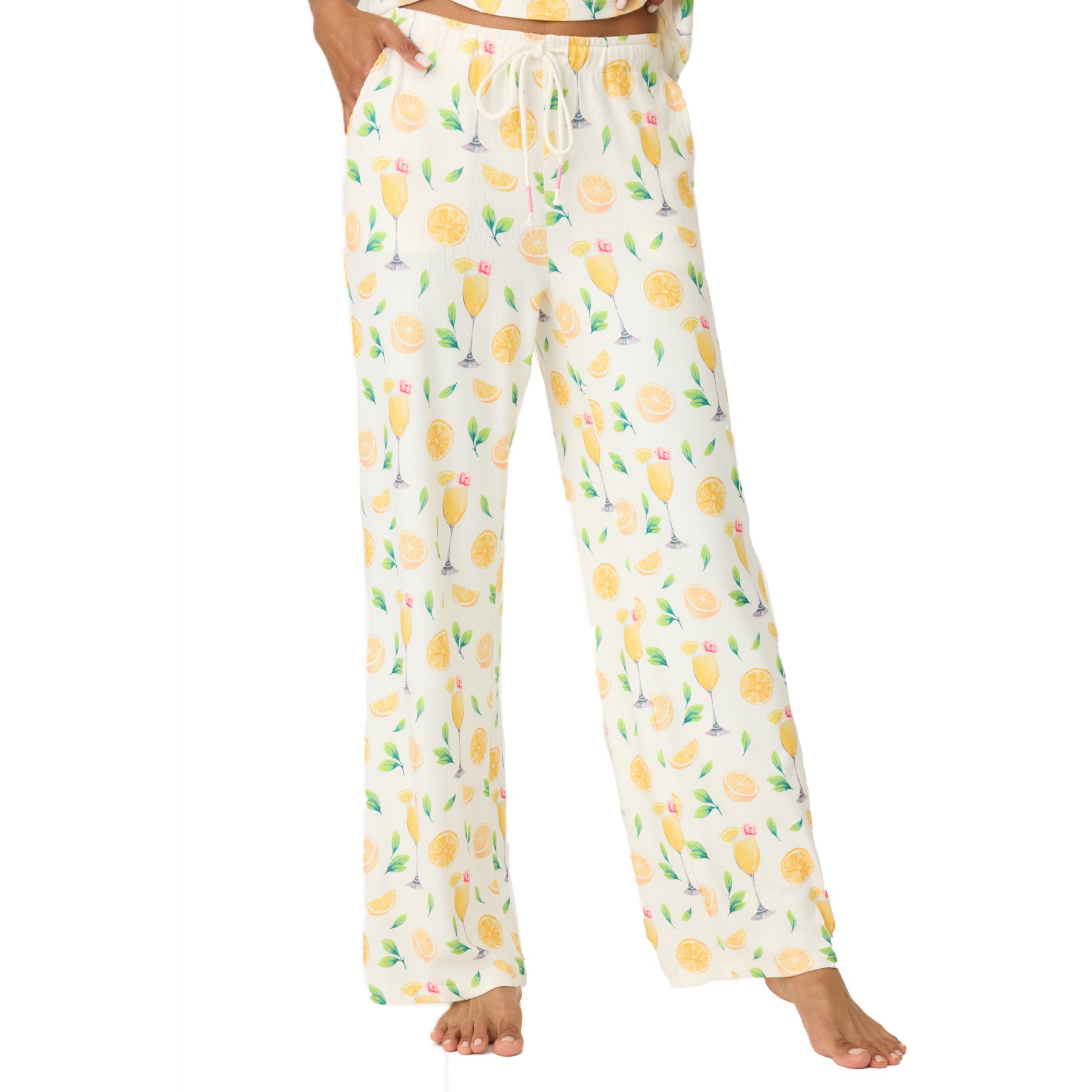 Woman wearing wide-leg ivory pyjama pants printed with lemons, green leaves, and mimosa glasses, shown from waist to feet.