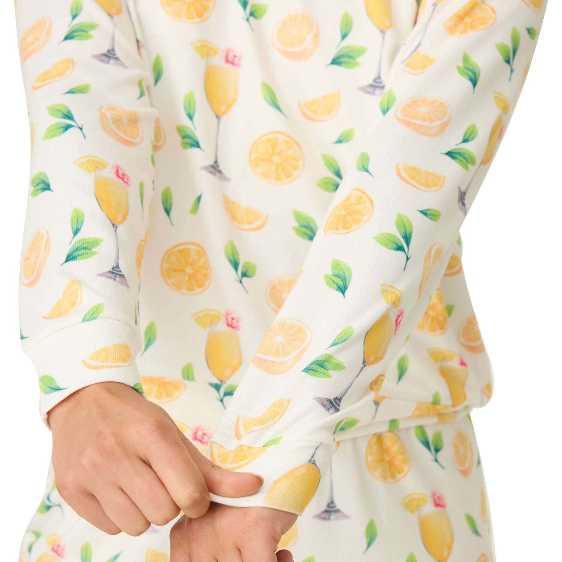 Close-up of a person adjusting the cuff of a long-sleeve ivory top featuring an all-over mimosa and lemon print, paired with matching pants.