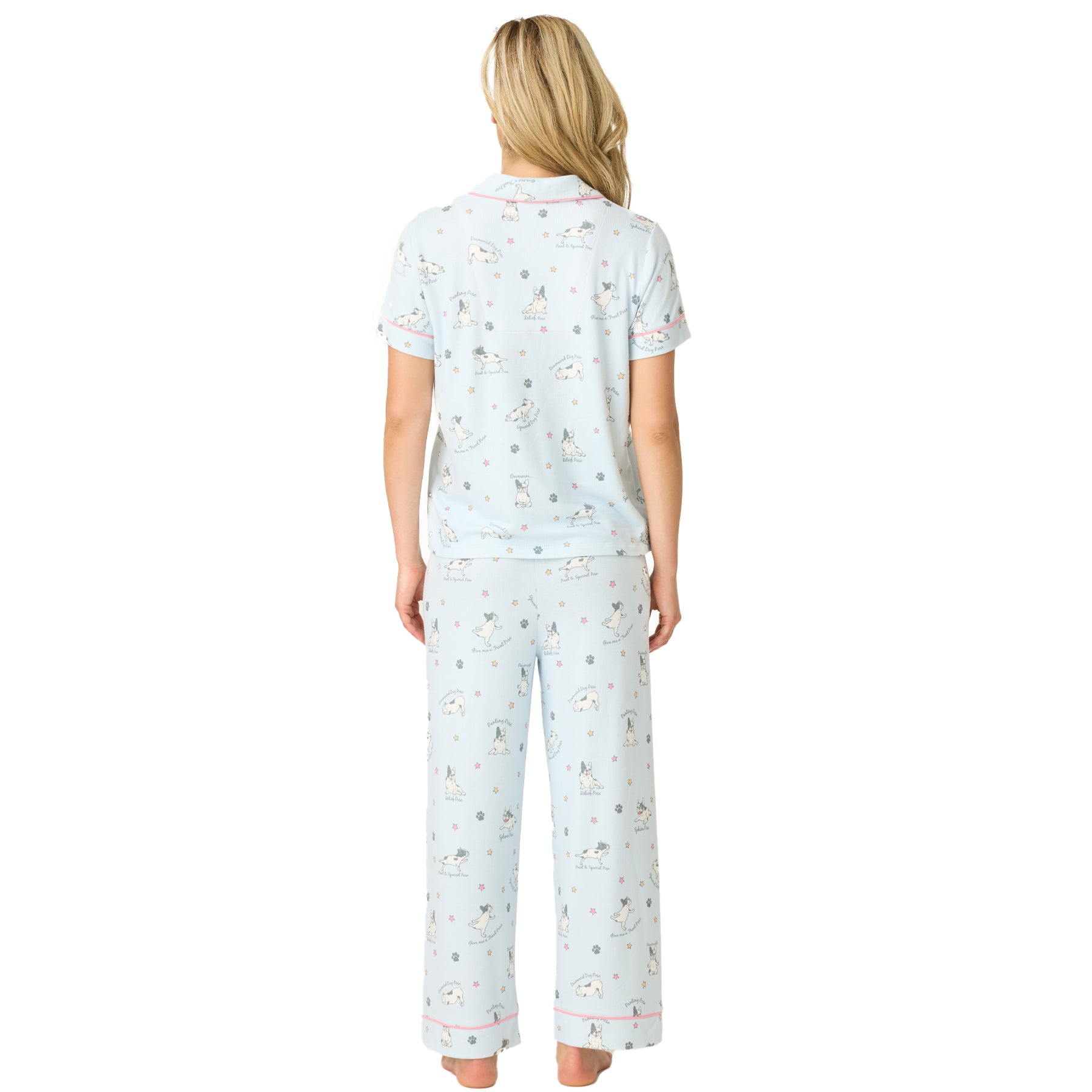 Back view of a woman wearing a light blue pyjama set with short sleeves and wide-leg pants, printed with cartoon French bulldogs, paw prints, and stars.