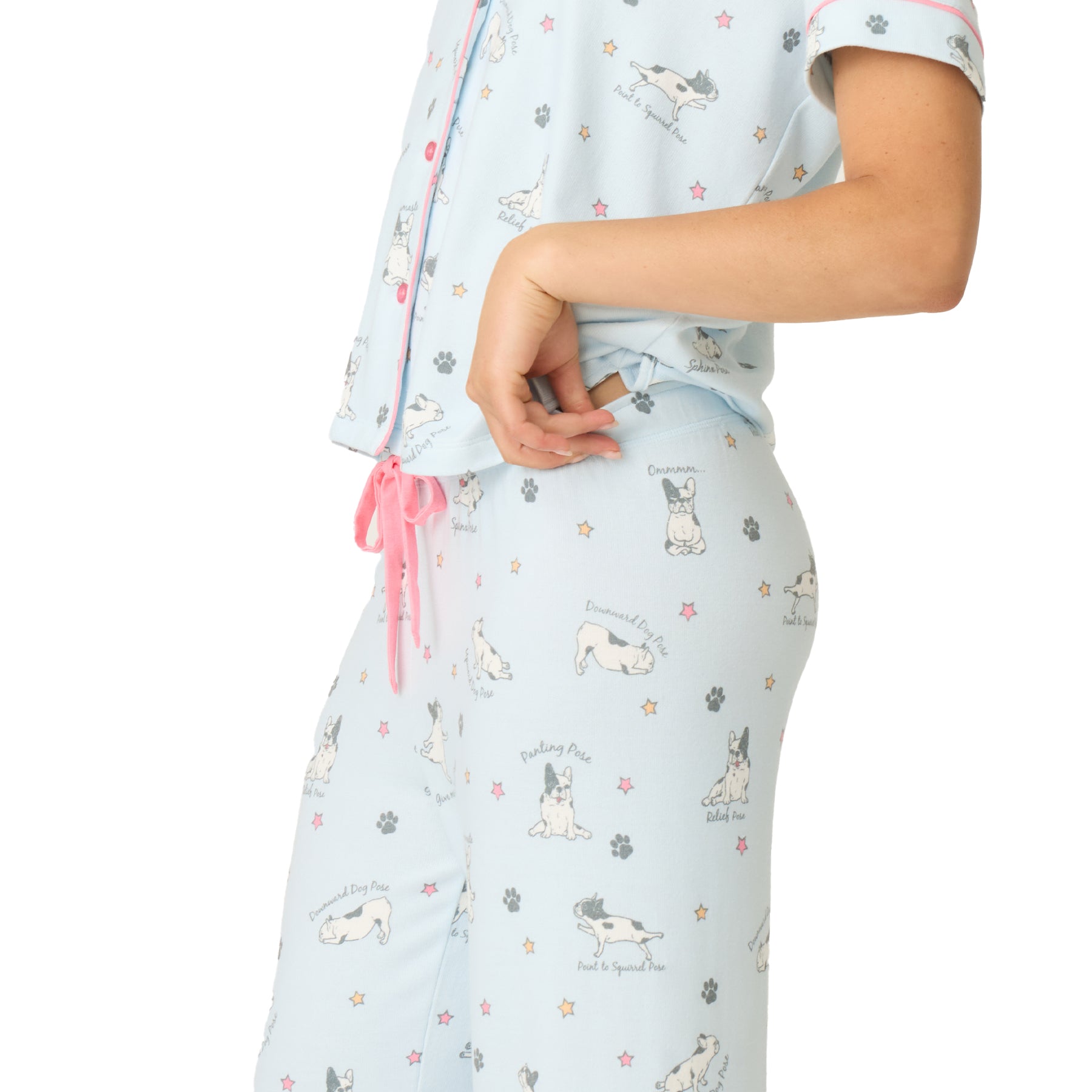 Close-up of a woman’s hip and waist in a light blue pyjama set, showing dog illustrations with pose names and pink drawstring waist detail.