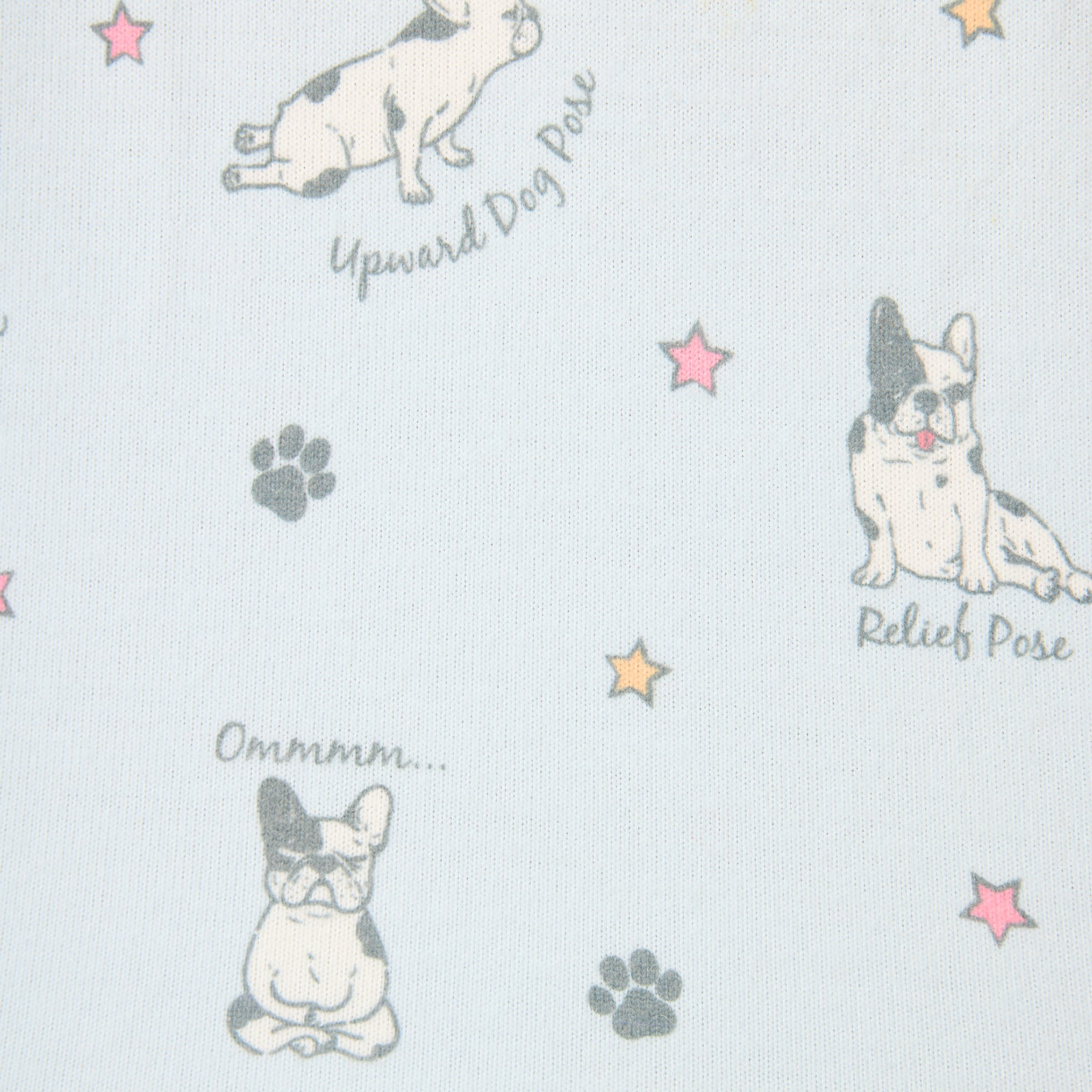 Close-up of soft light blue fabric printed with cute French bulldogs doing yoga poses such as “Relief Pose” and “Upward Dog Pose,” surrounded by colourful stars and paw prints.