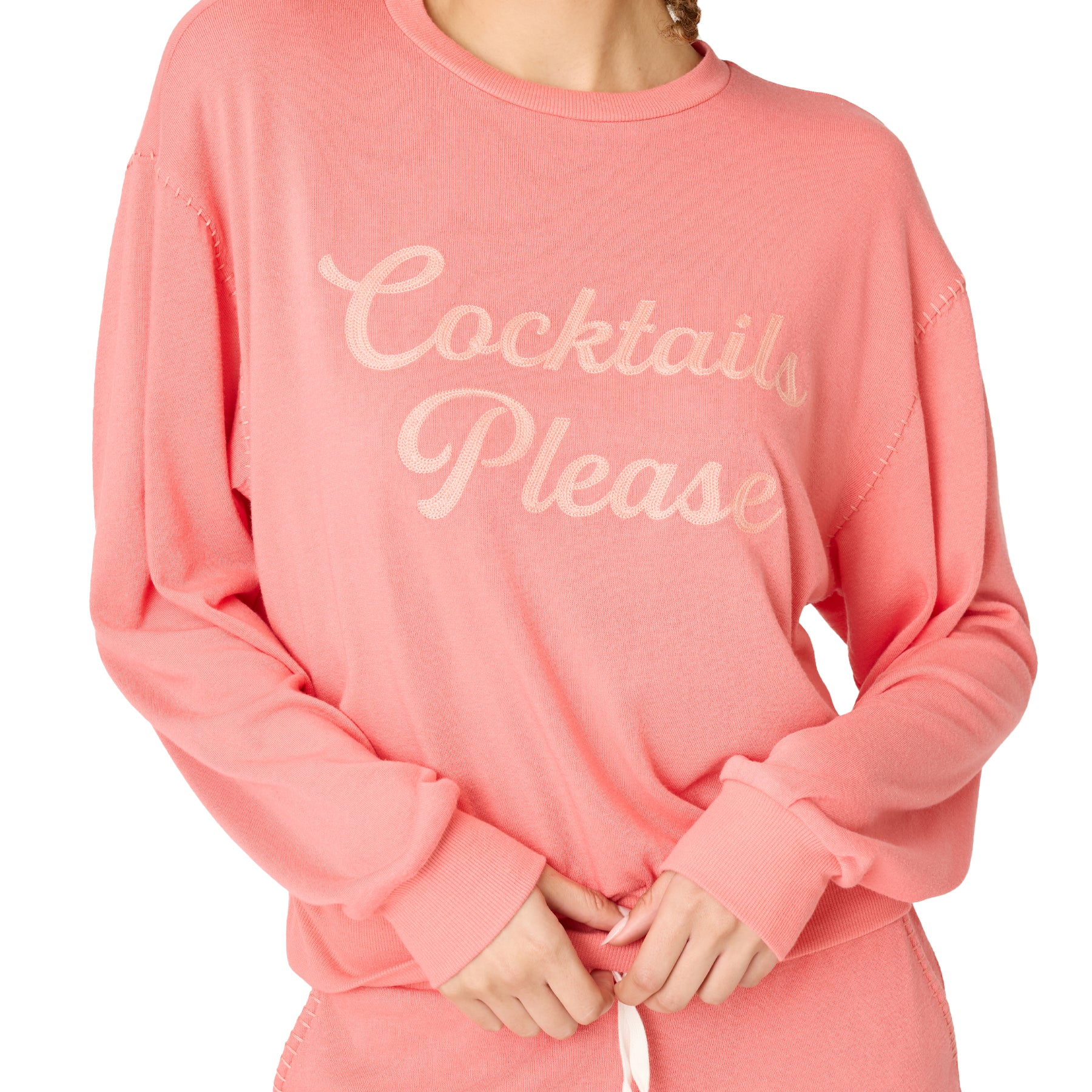 Close-up of coral sweatshirt with “Cocktails Please” slogan and soft knit fabric detail.