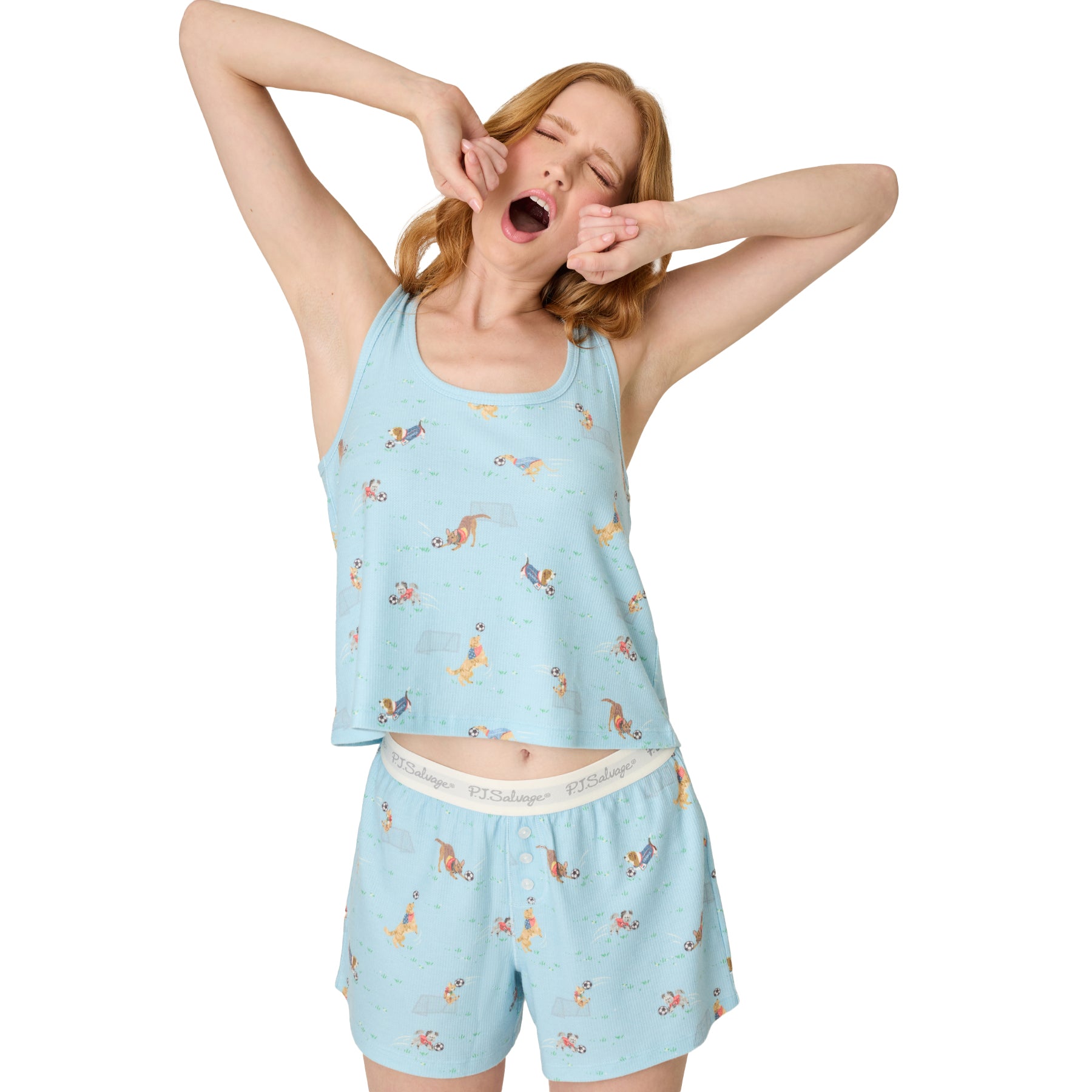 Woman wearing light blue PJ Salvage tank and shorts set with playful dog and soccer print, stretching pose on white background
