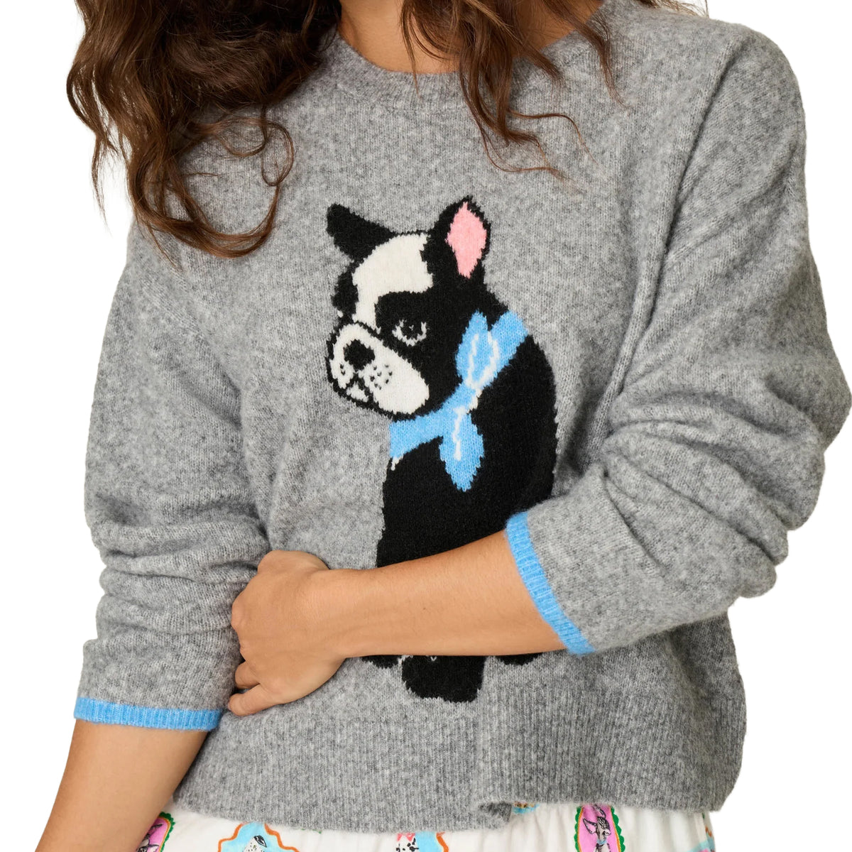 A woman wearing a heather gray knit sweater with a large black-and-white dog graphic on the front, a light blue bow tie, and light blue ribbed trim on the cuffs.