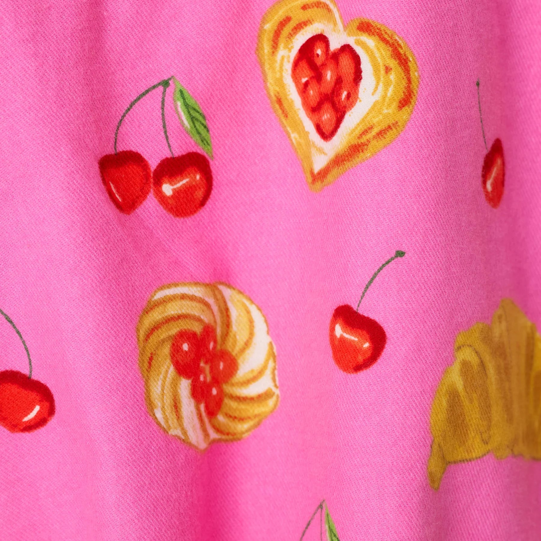 Close-up of pink sleepwear fabric featuring colorful cherries, croissants and heart-shaped pastry illustrations.