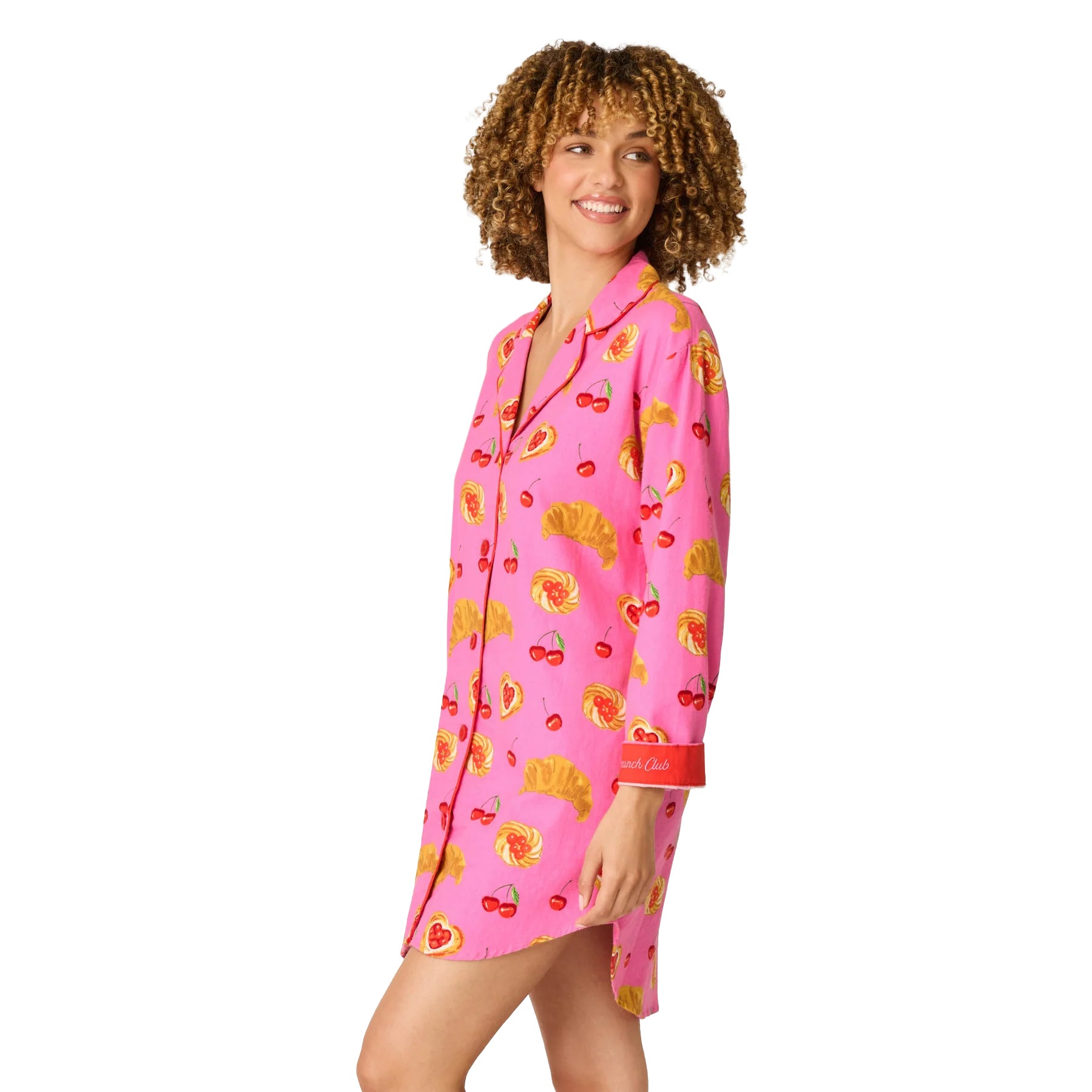 A woman modeling a pink long-sleeve pajama shirt with a colorful fruit and pastry print, set against a plain white background.