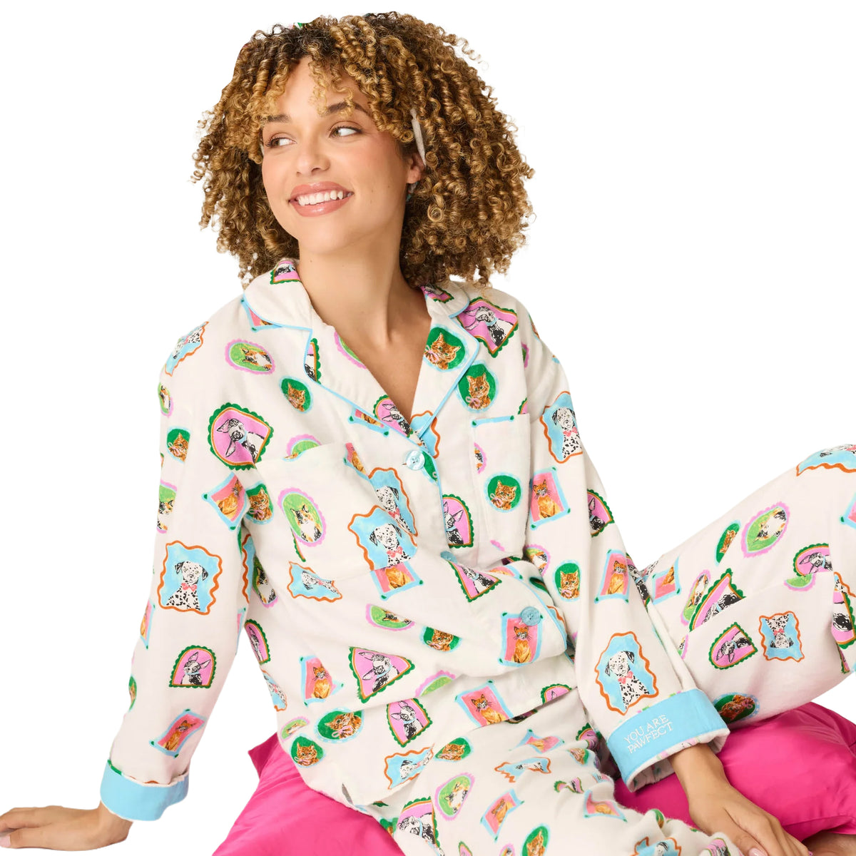 Woman wearing cream dog and cat print pajamas with blue piping, seated on a bright pink cushion.
