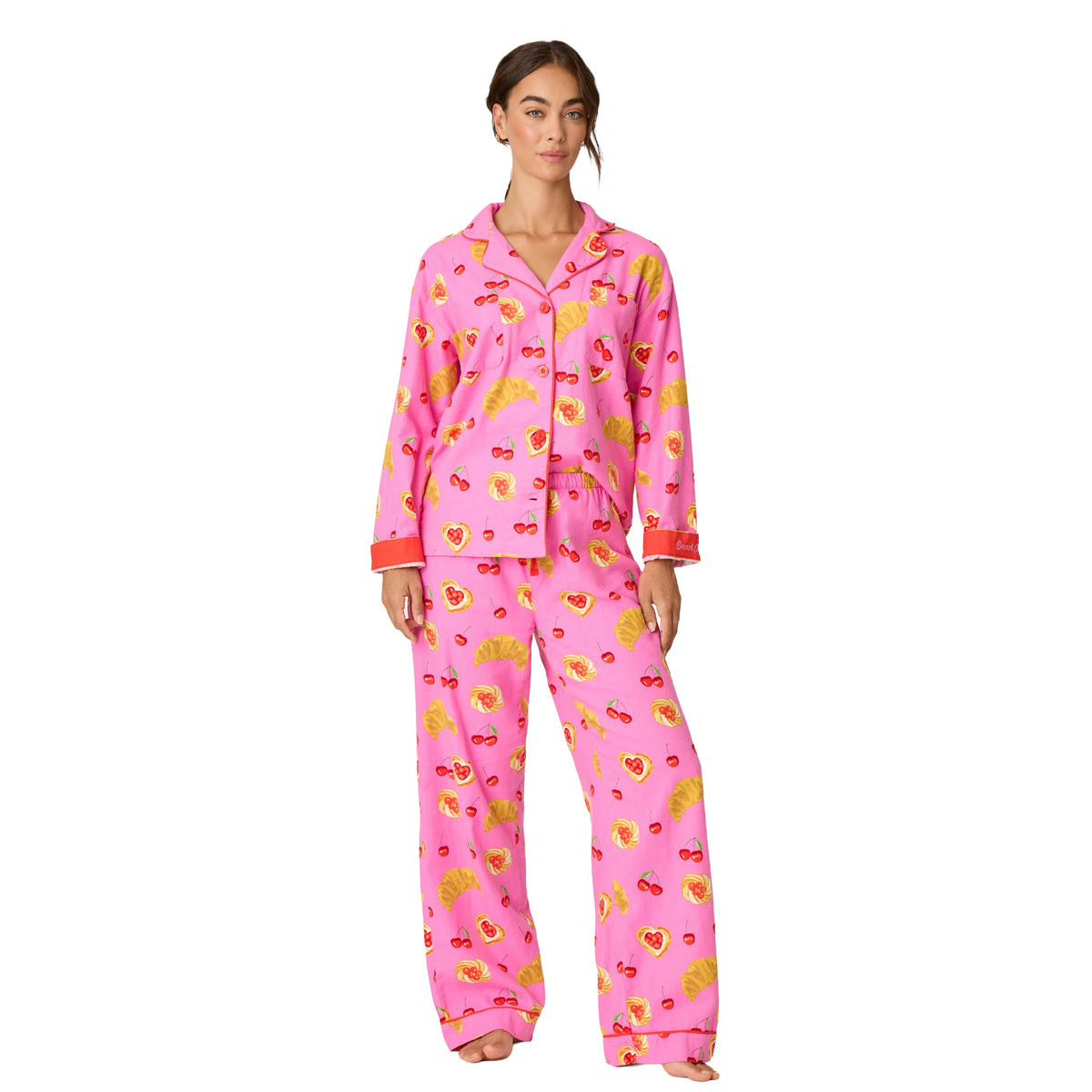 Front view of bright pink button-up pajama set with cherry and pastry print, red piping and relaxed wide-leg pants.
