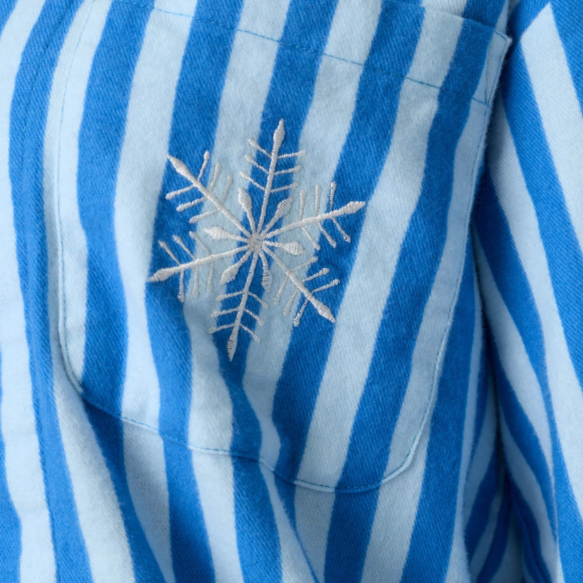Close-up of white embroidered snowflake on the chest pocket of blue and white striped flannel pajamas.