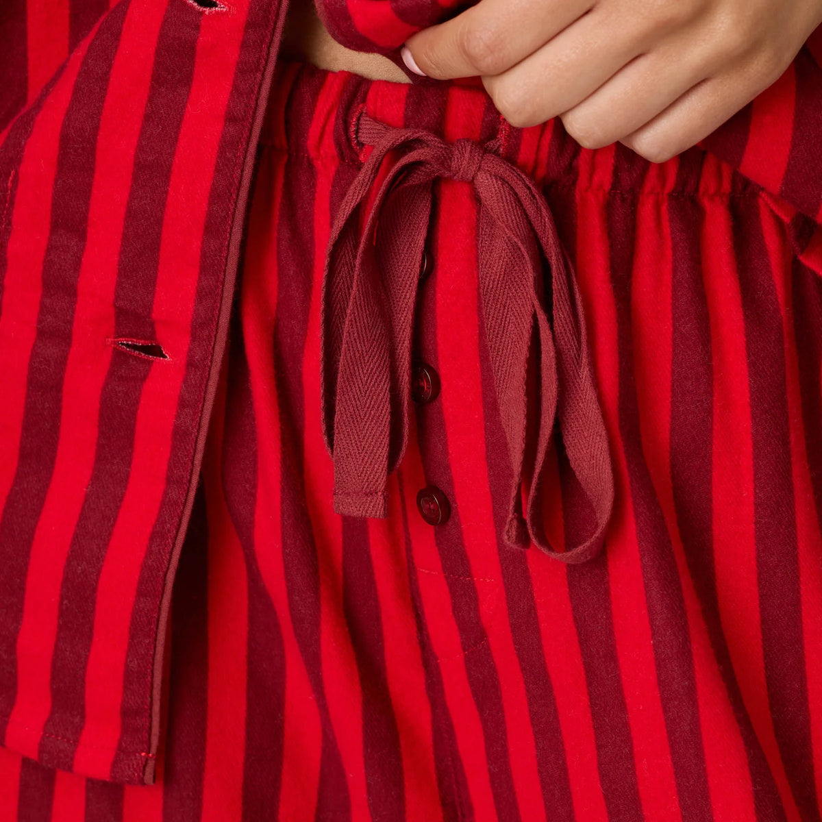 Close-up of red and burgundy striped flannel pajama pants featuring an adjustable drawstring waistband and button fly.