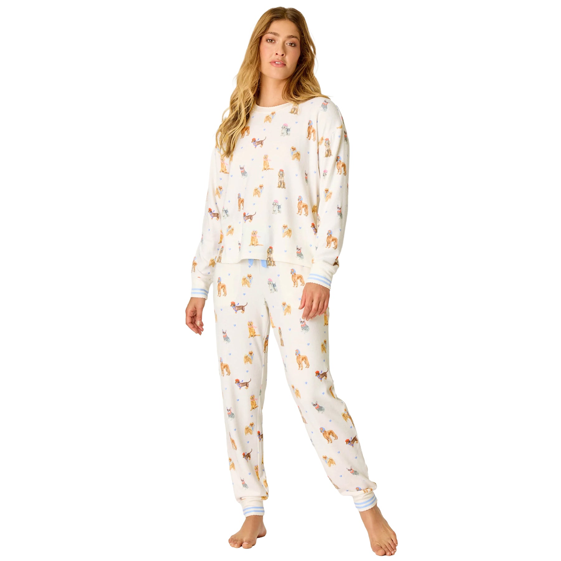 Woman wearing an ivory long-sleeve pajama set with a playful French dog print, blue heart accents and striped cuffs.