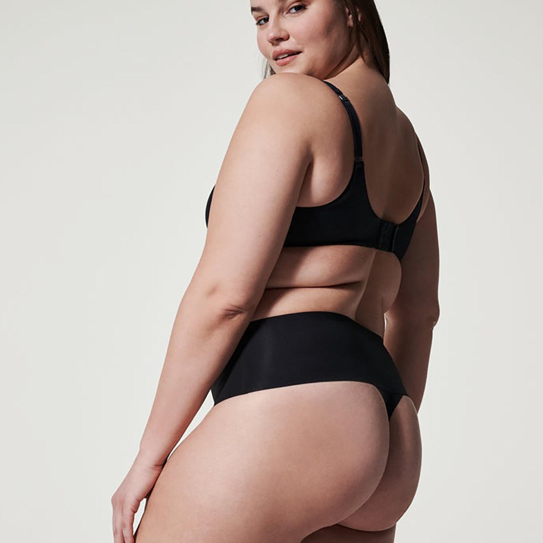 Side angle of SPANX black seamless thong showing high-rise waistband for tummy control and smooth finish.