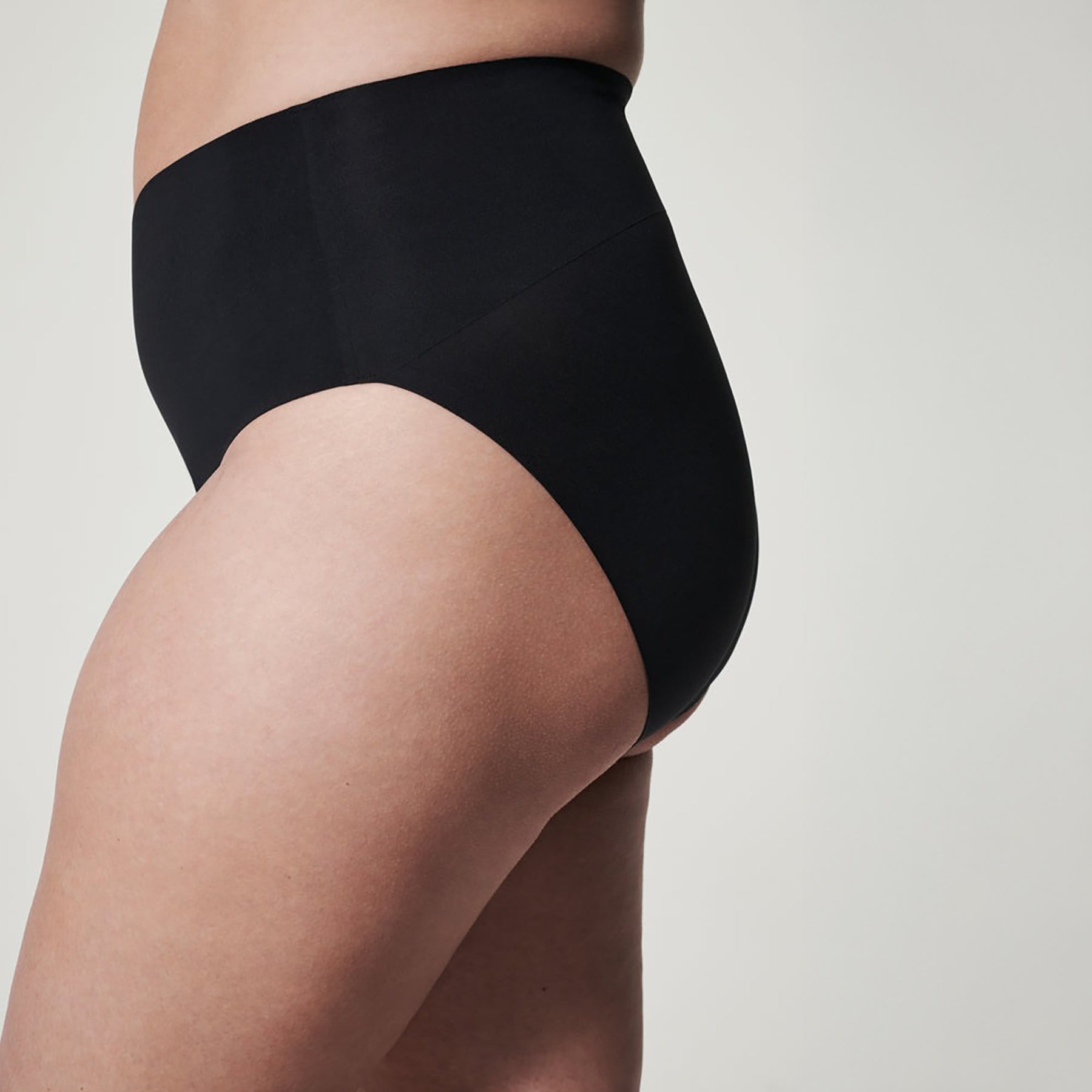 Side view of SPANX seamless shaping brief in black featuring high-rise compression waistband for a flattering silhouette.
