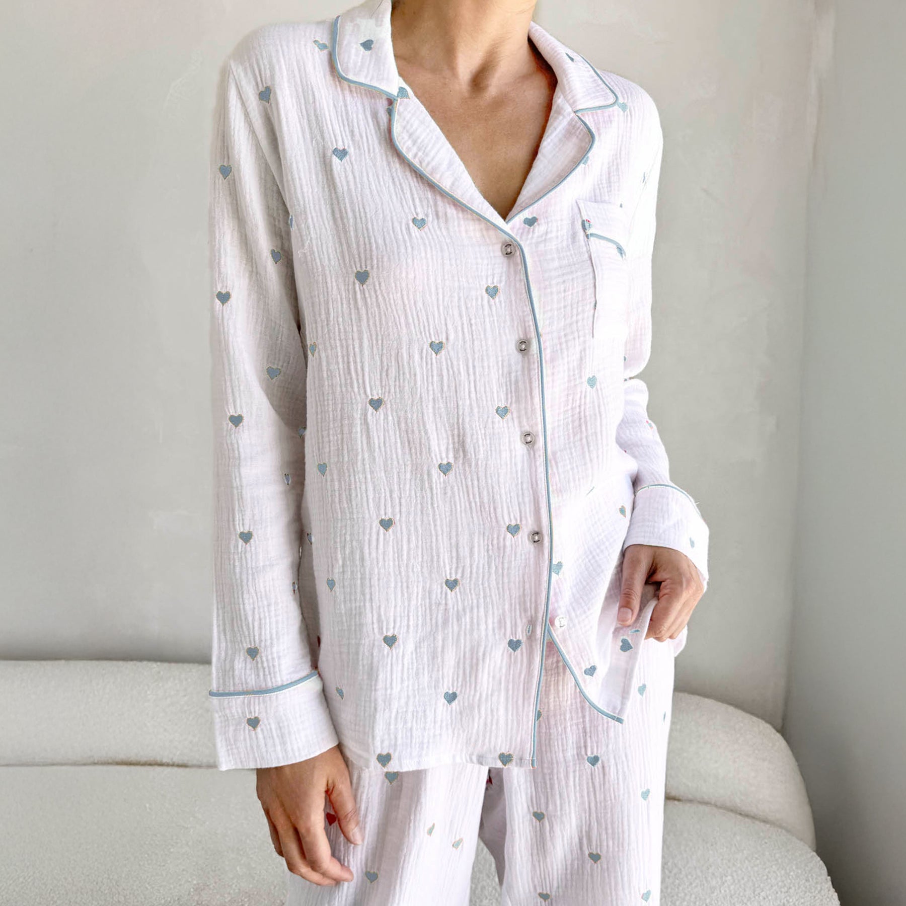 classic button up pyjama set in crinkle cotton in white with mini bleached indigo light blue embroidered hearts. Matching bleached indigo light blue contrast piping on trims. Front view close up on model.