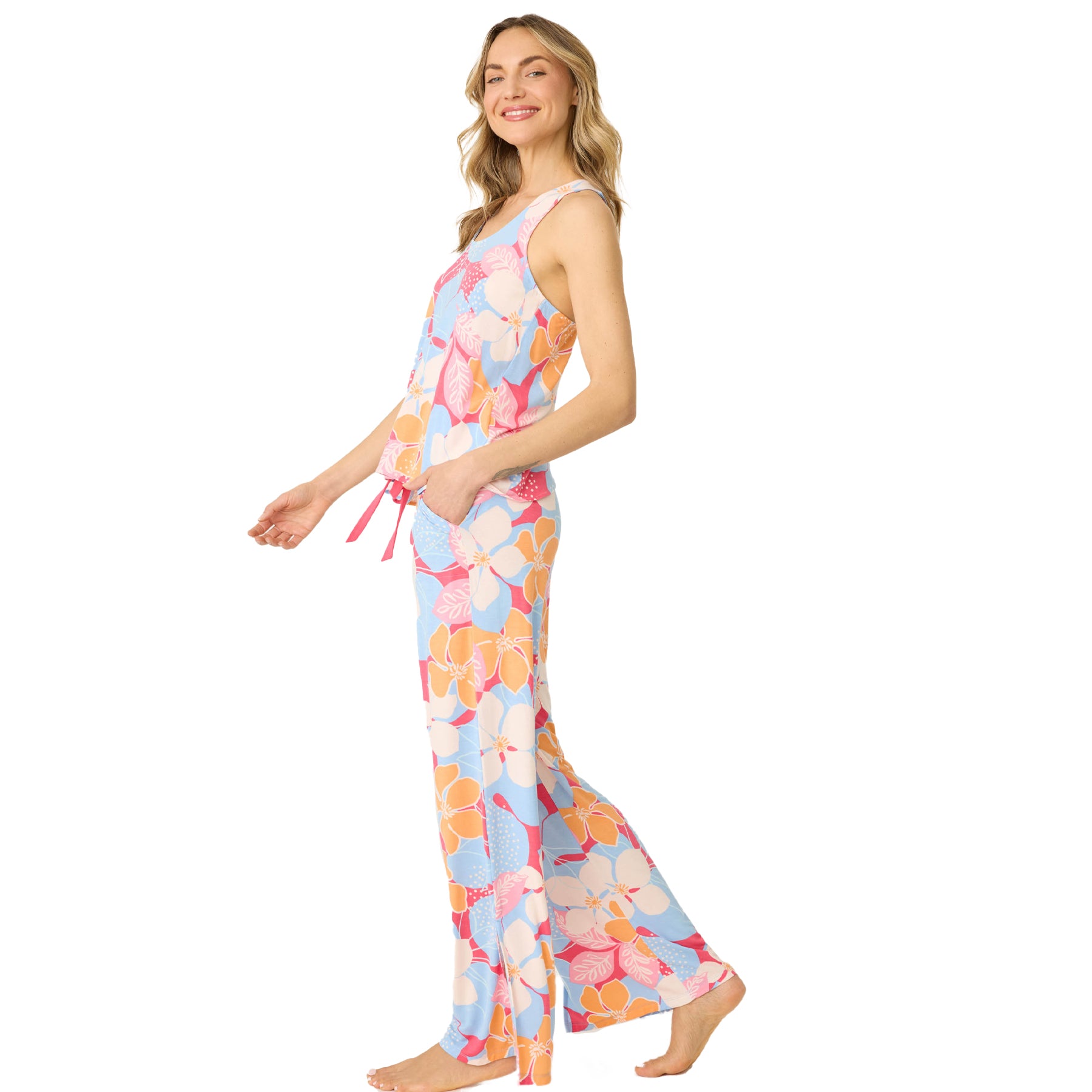 Side view of a woman in a colorful floral tank and pajama pants set, smiling and walking barefoot.