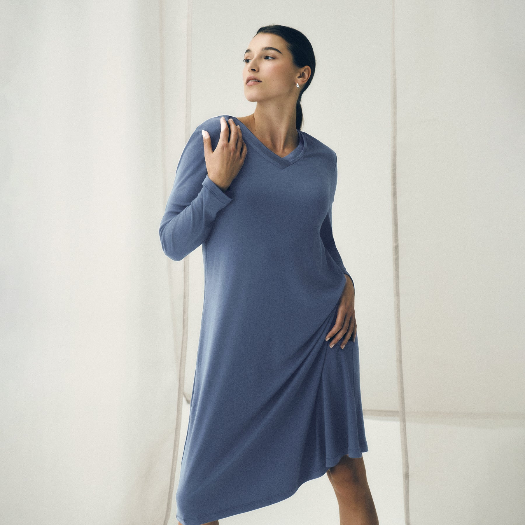 Woman modelling a soft blue long-sleeve nightgown with a satin V-neckline and flowing midi-length silhouette.