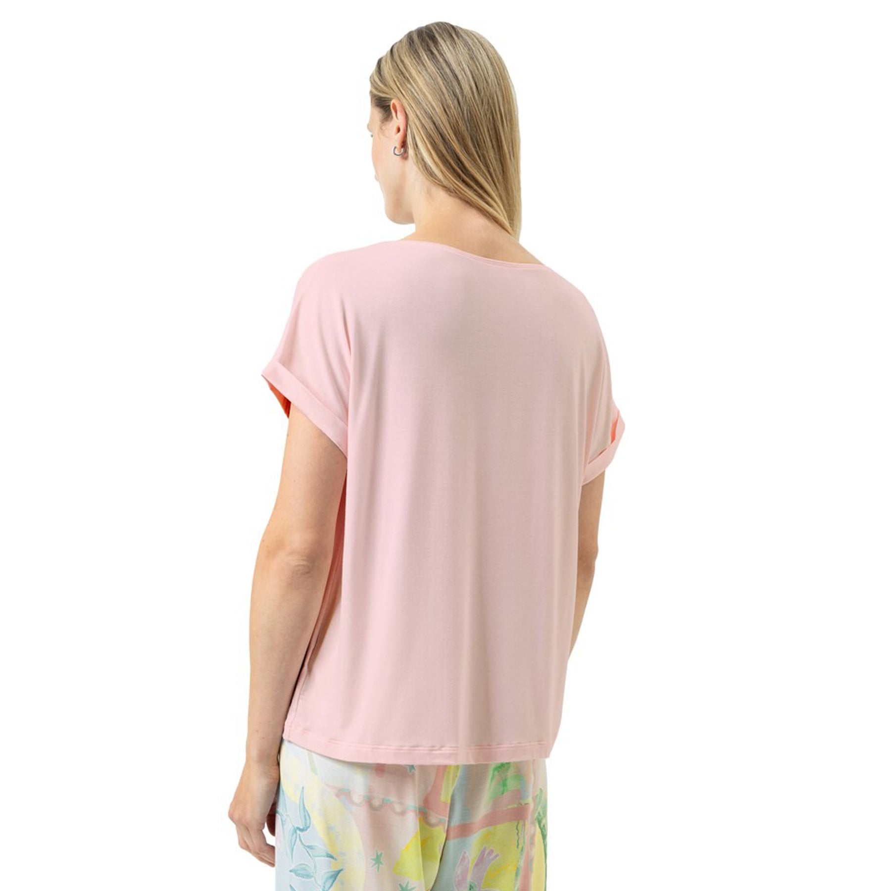 Back view of a woman wearing a relaxed-fit soft pink short-sleeve T-shirt with rolled cuffs, styled with printed lounge pants.