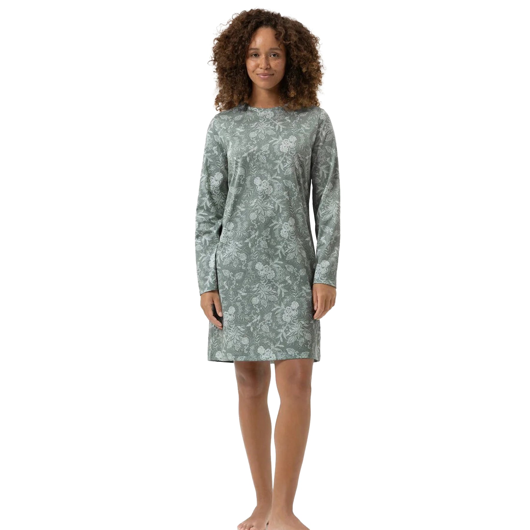 Woman wearing a sage green long-sleeve nightshirt with a white floral pattern, standing barefoot.