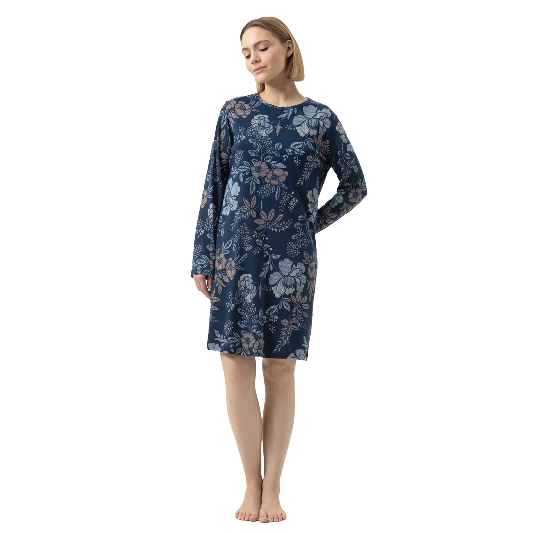 Woman wearing a navy blue floral long-sleeve nightgown, standing barefoot with hands behind her back.