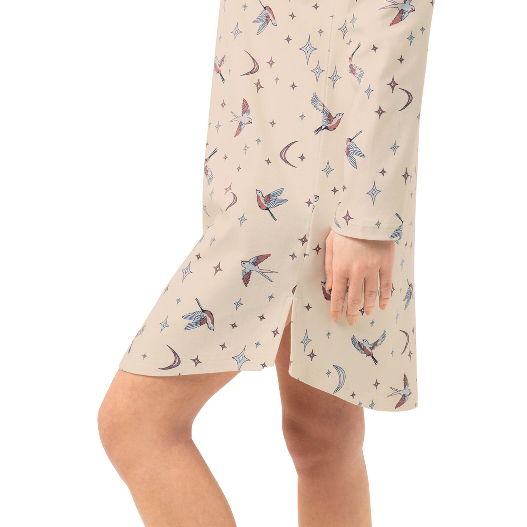 Close-up of cream nightgown showing the colourful flying bird, crescent moon and star print with a small side slit at the hem.