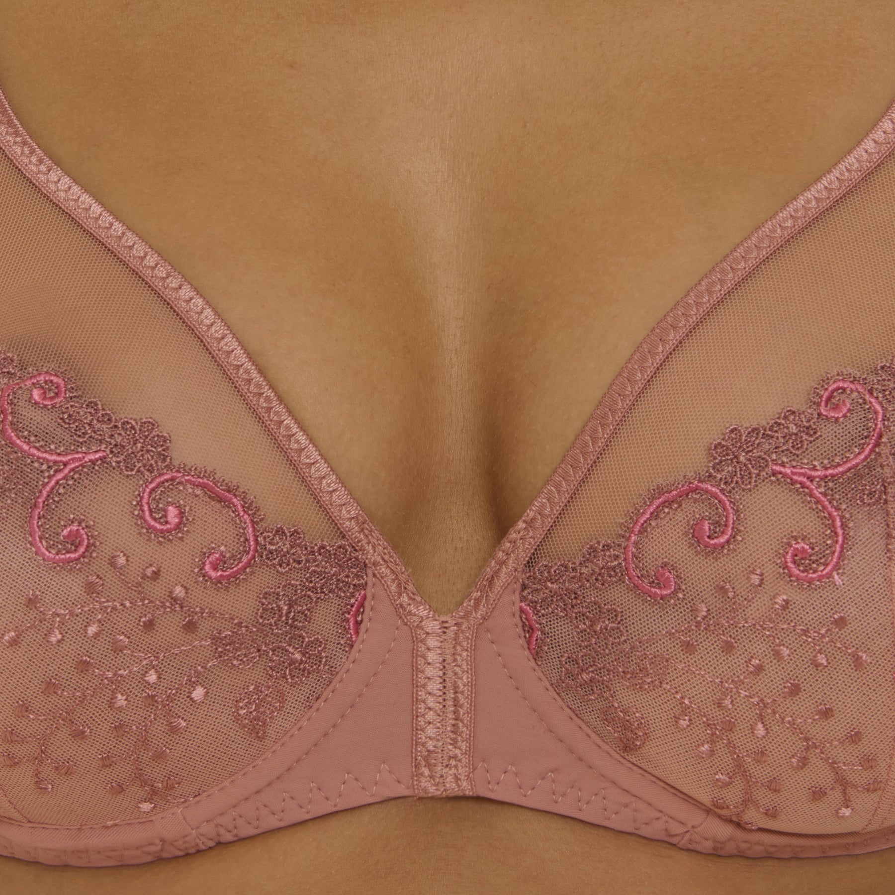 Close-up detail of pink sheer lace bra cups featuring delicate floral embroidery and fine mesh fabric.