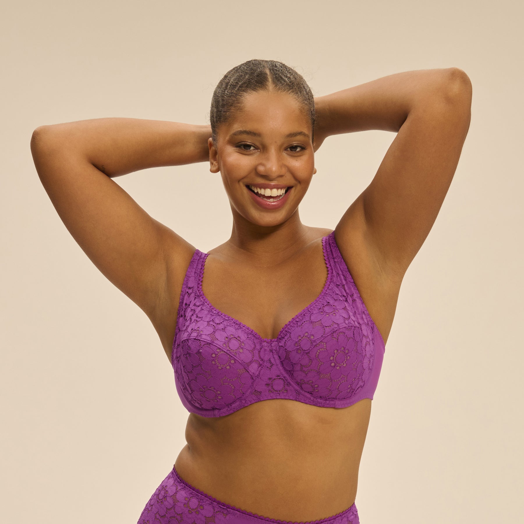 Close-up of model wearing Simone Pérèle Oisive Full Cup Bra in fuchsia lace, with arms lifted behind head and smiling.