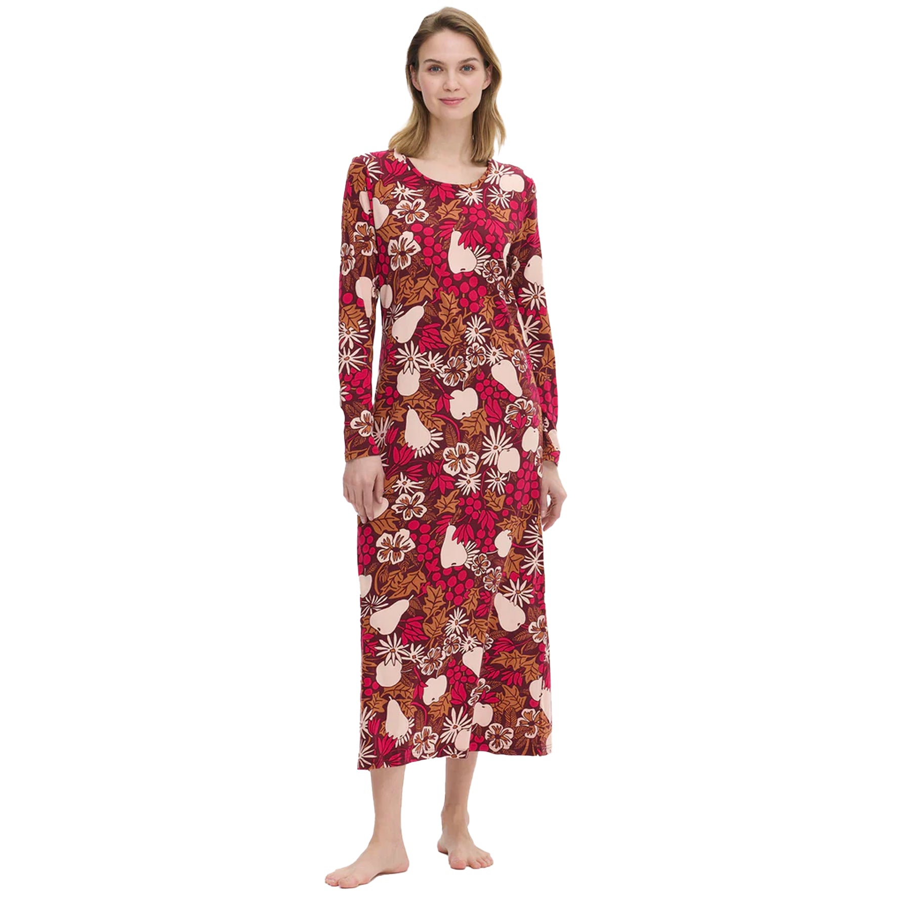 Woman wearing a long burgundy nightdress with a vibrant fruit and floral print in pink, beige, and brown tones, standing barefoot against a white background.