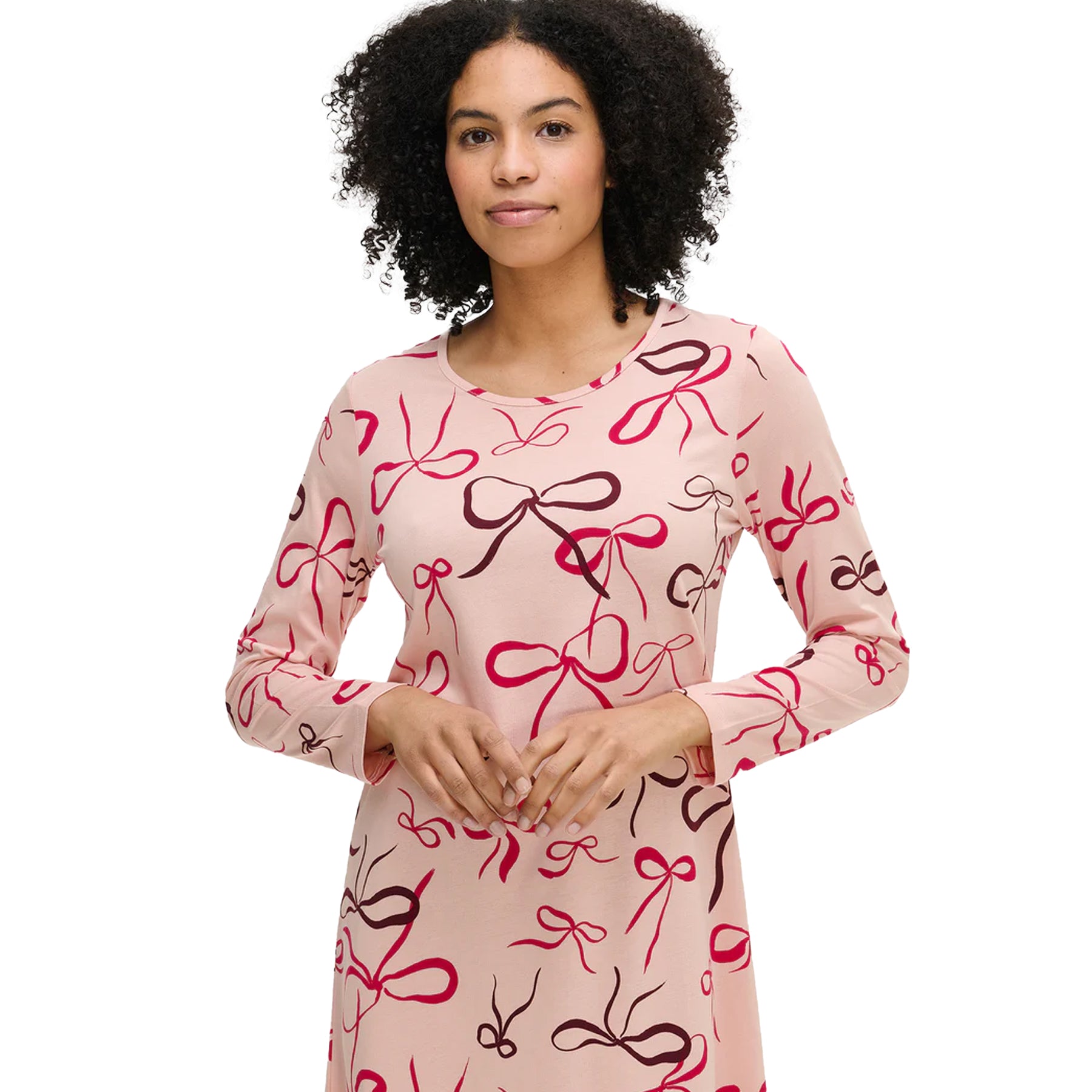 Woman wearing a pink cotton nightdress with multicolour bow pattern and round neckline detail.