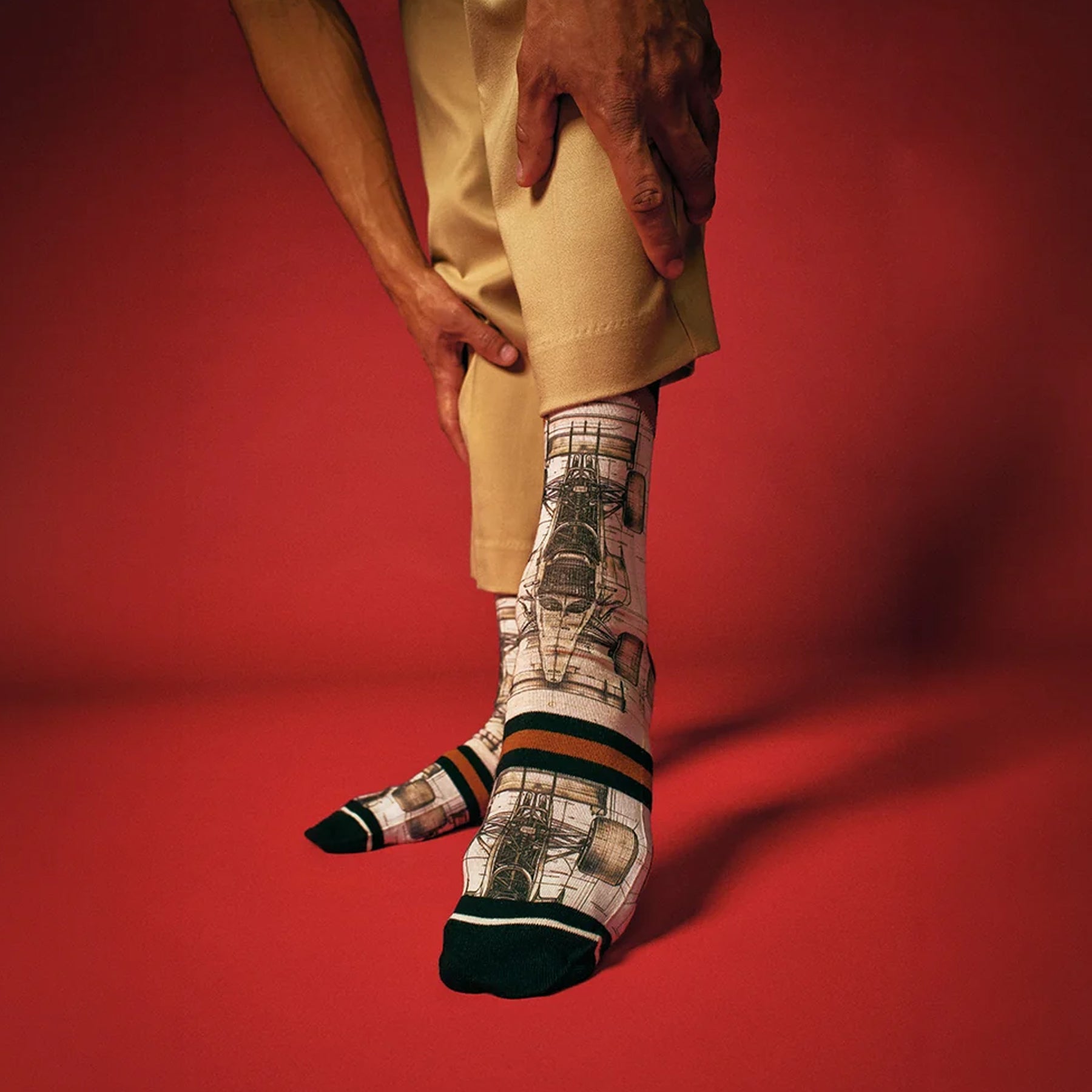 Model wearing Formula 1 race car print crew socks with black and rust stripe accents against a bold red background.