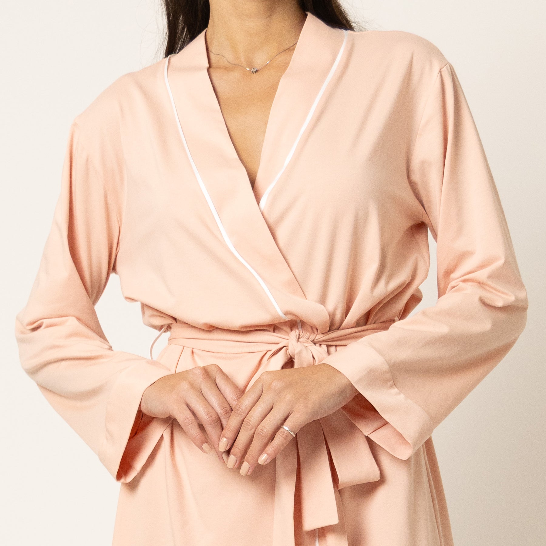 Close-up of blush pink robe with white trim, shawl collar neckline and tied waist detail