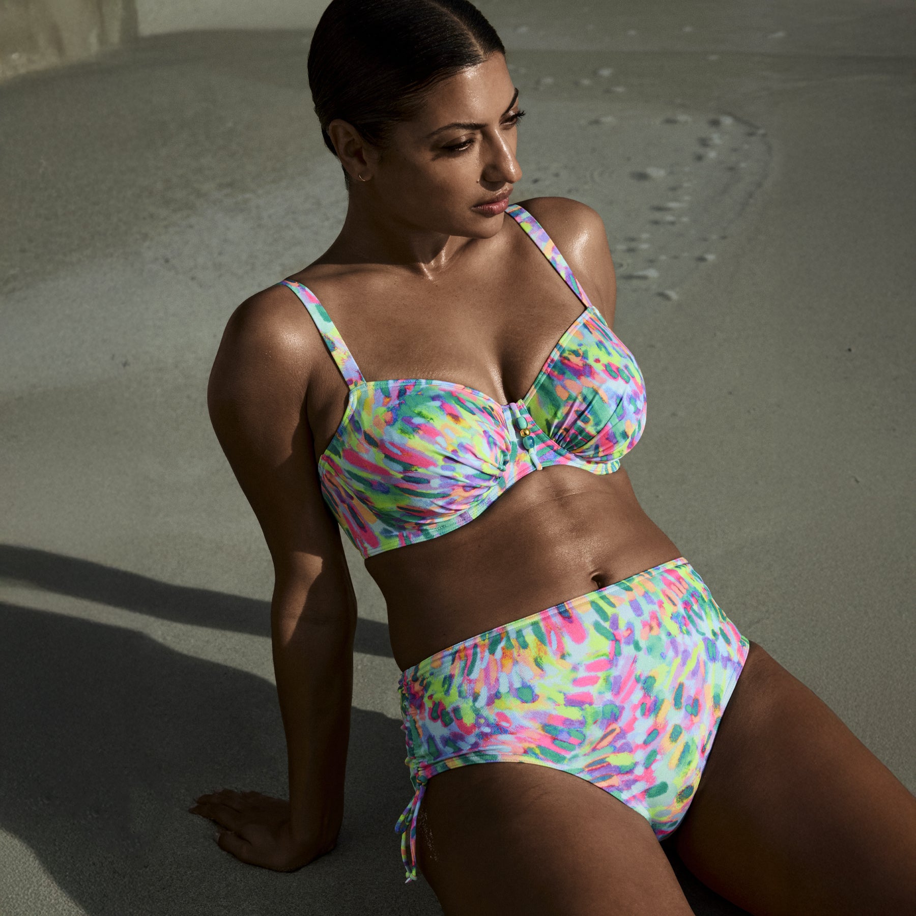 Model lounging on the beach in vibrant abstract print bikini set with ruched cups – style 401-4052.